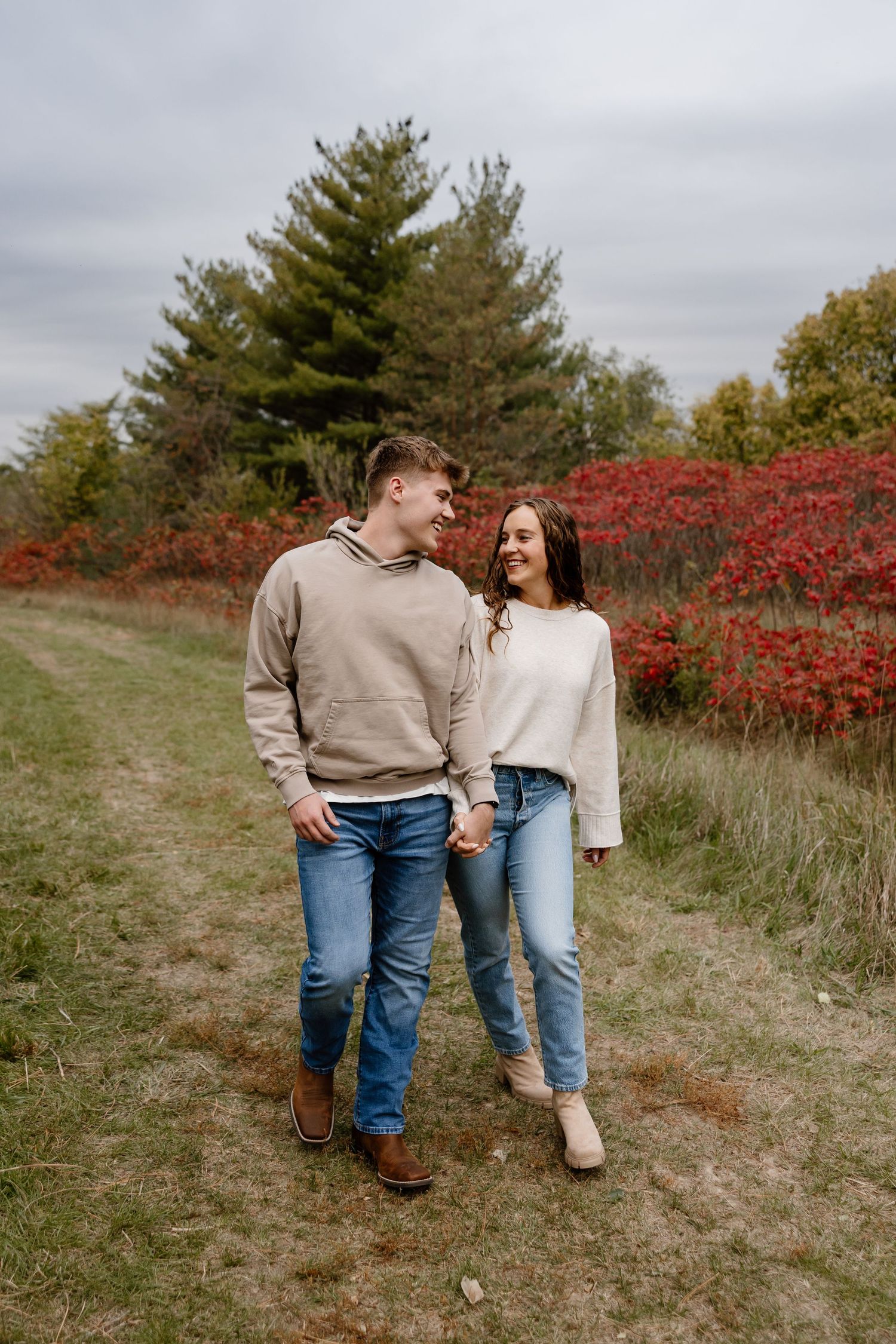 Couple walking together on autumn path with red foliage in background.