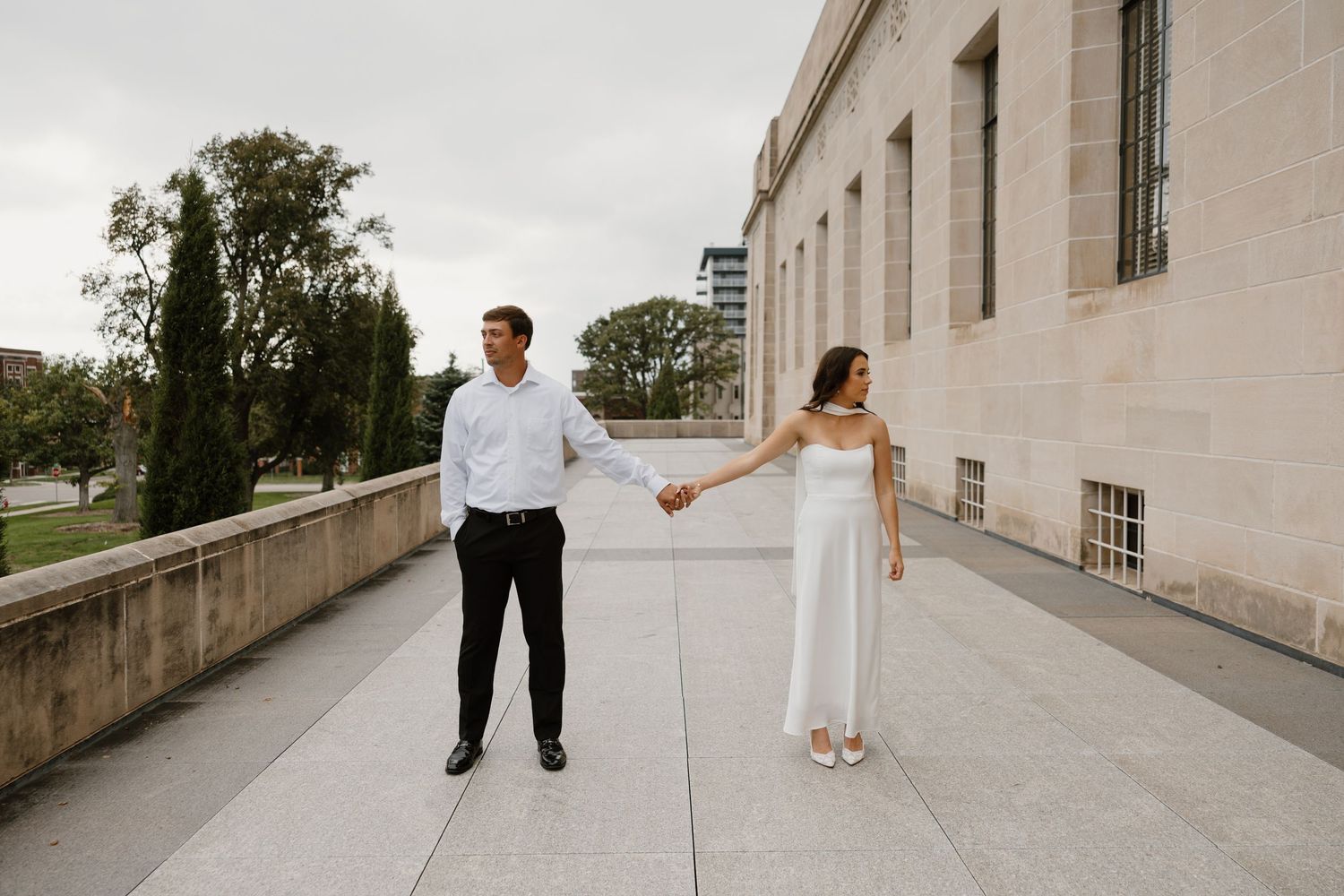 Couple walks together along stone pathway outside classical building architecture.