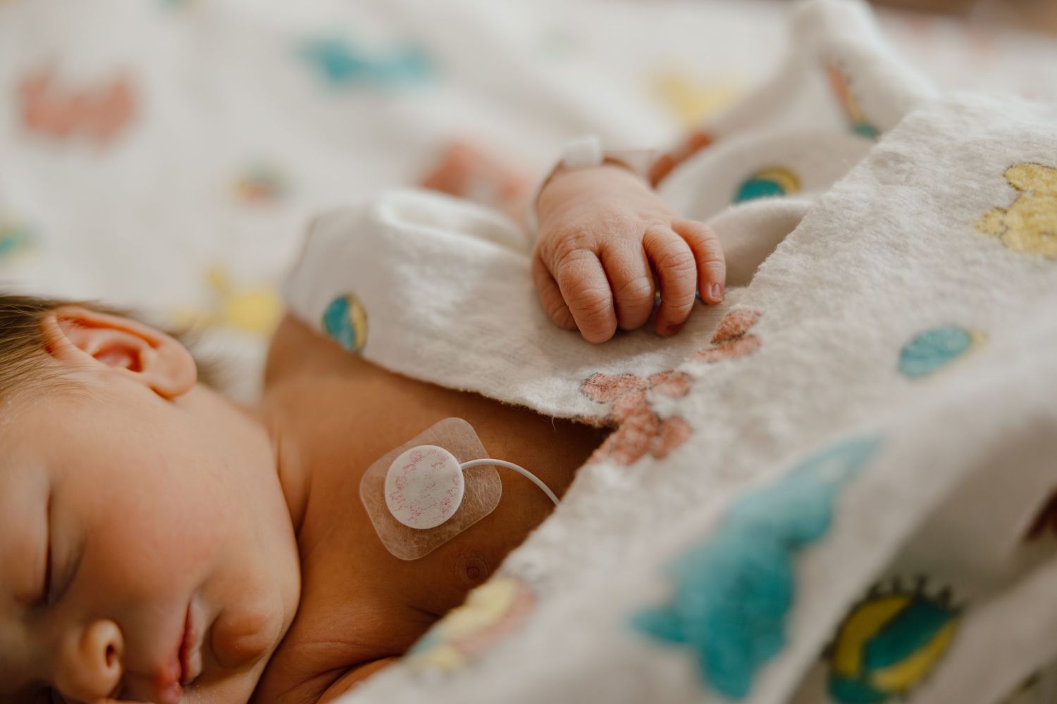 Newborn baby sleeping peacefully on patterned hospital blanket.