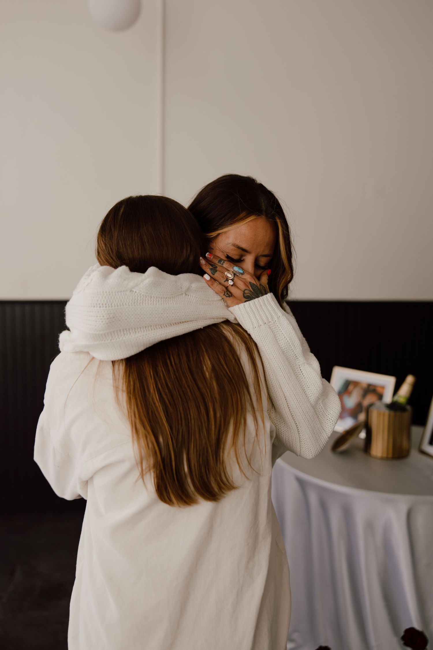 Two people share a warm embrace in a minimalist indoor setting.