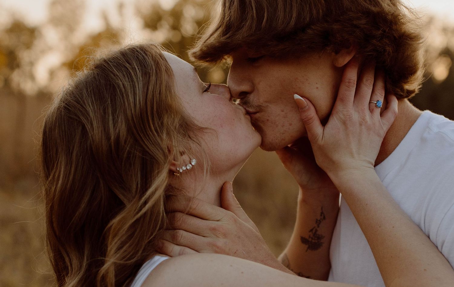 A romantic couple sharing a tender kiss in warm sunset lighting outdoors.