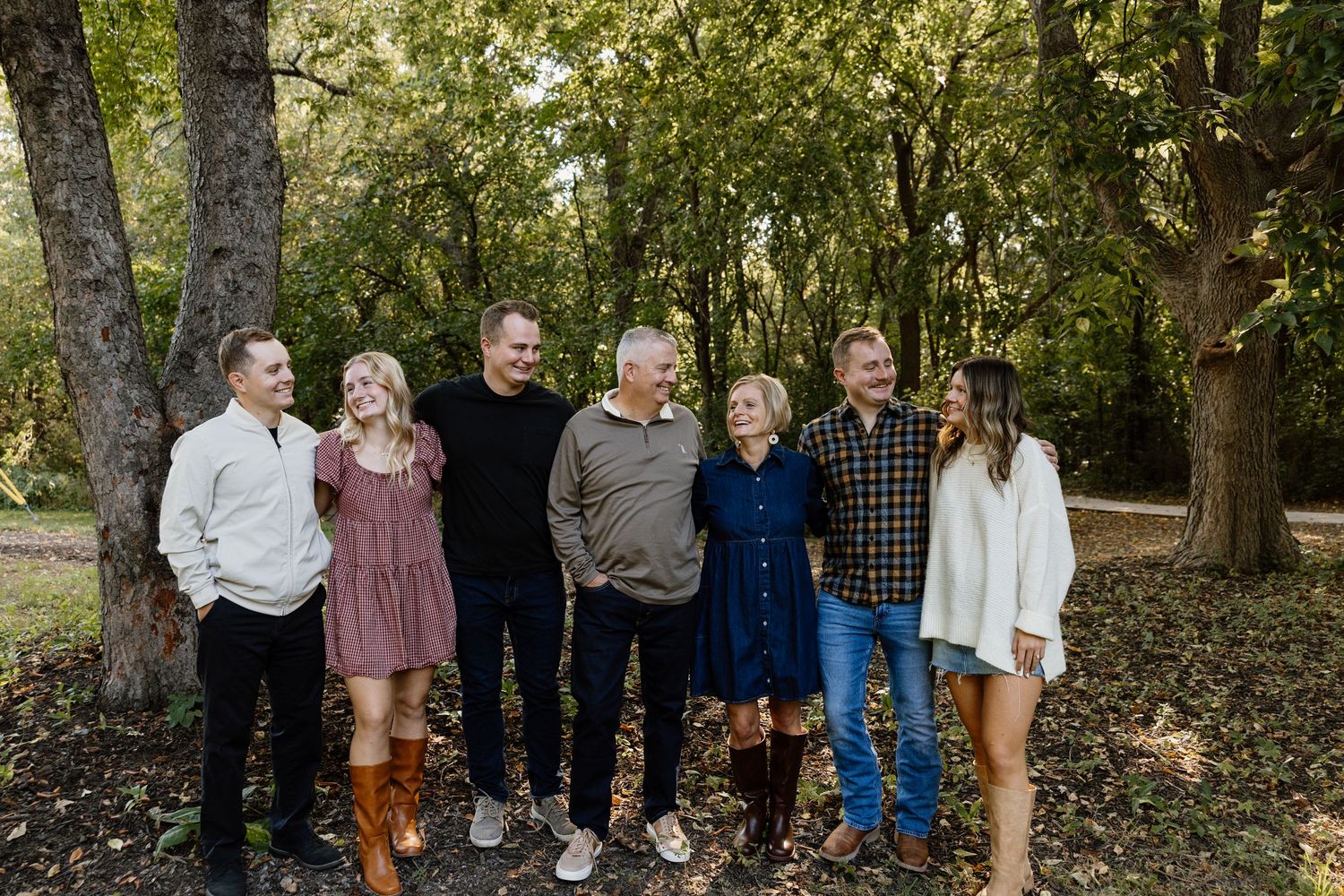 Large extended family group poses together outdoors among autumn trees.