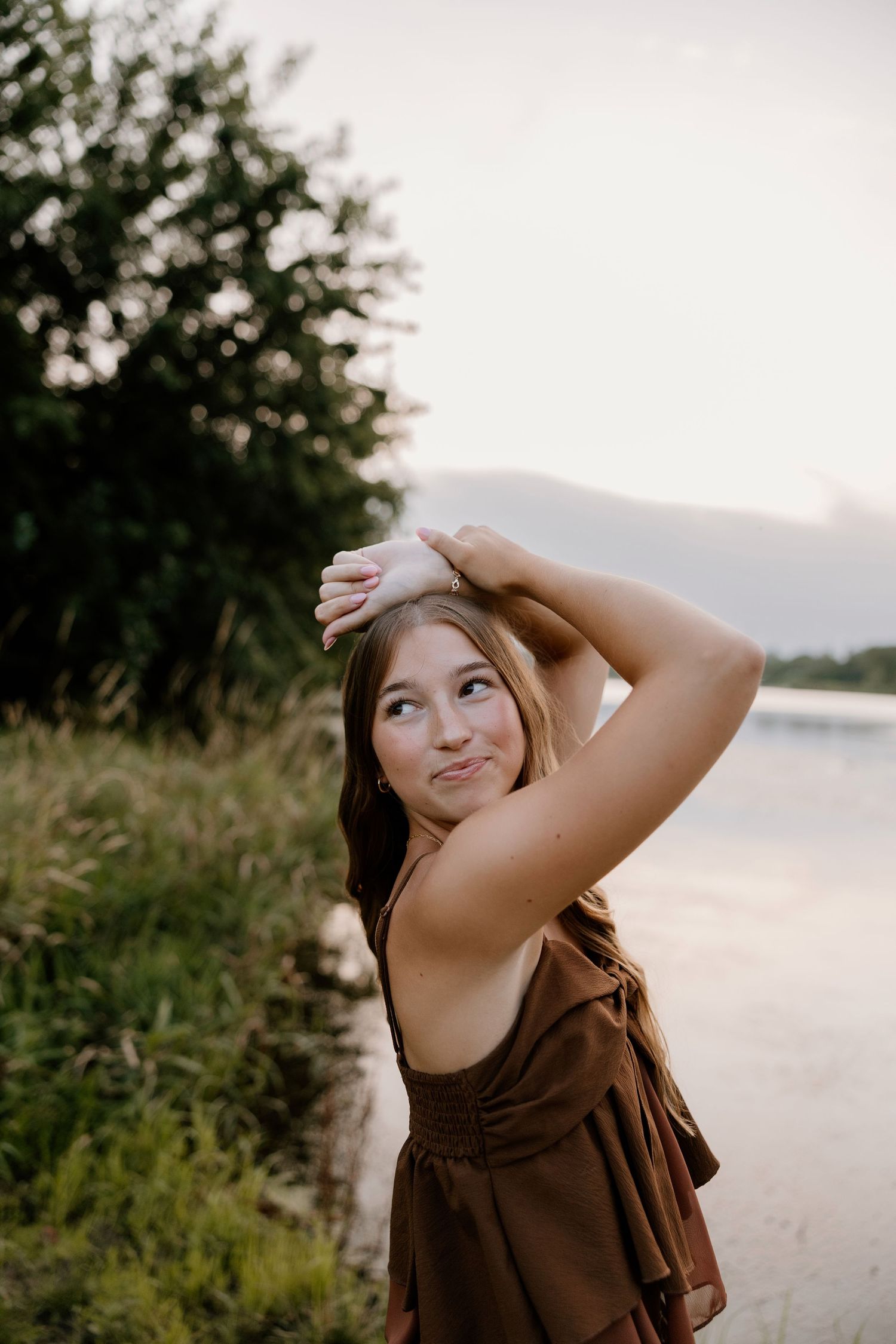 Artistic portrait by a lake during golden hour with trees and water in the background.