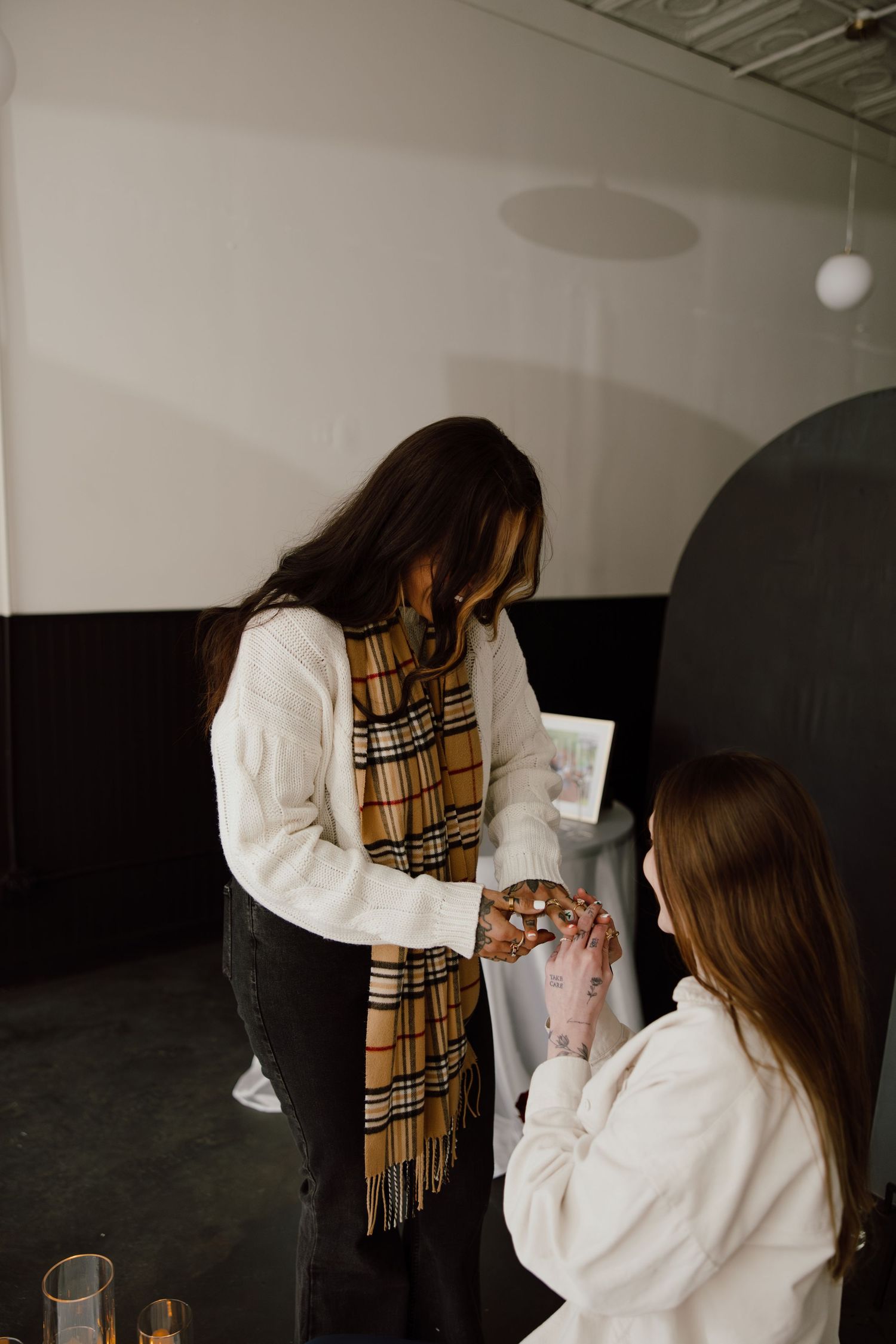 Friends in white sweaters and plaid scarves share a special moment indoors.