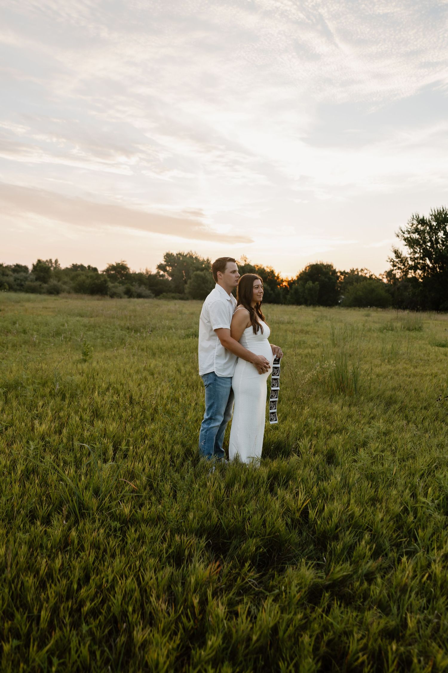 Couple embraces in a golden wheat field during sunset.