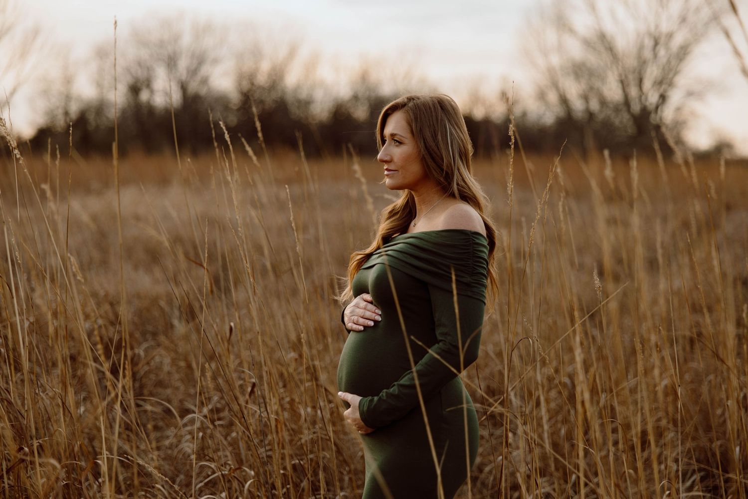 A maternity portrait in a field of tall grass during golden hour.