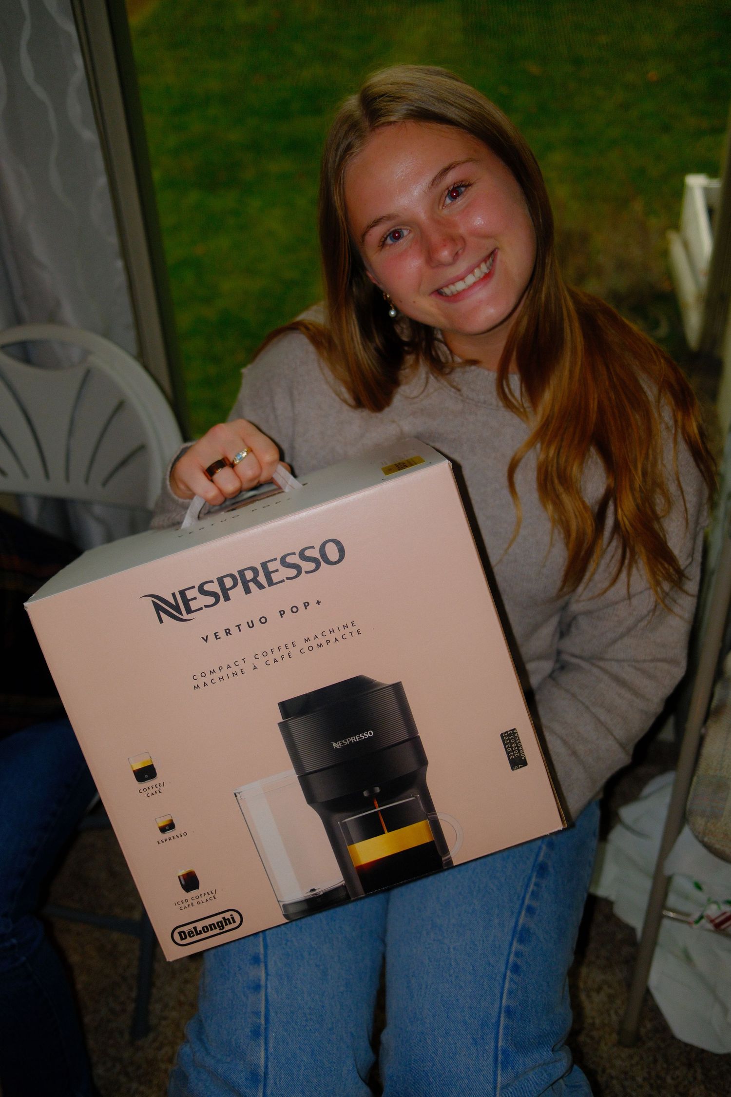 Someone holds a Nespresso Vertuo Next coffee maker box while sitting outdoors wearing jeans and a gray sweater.