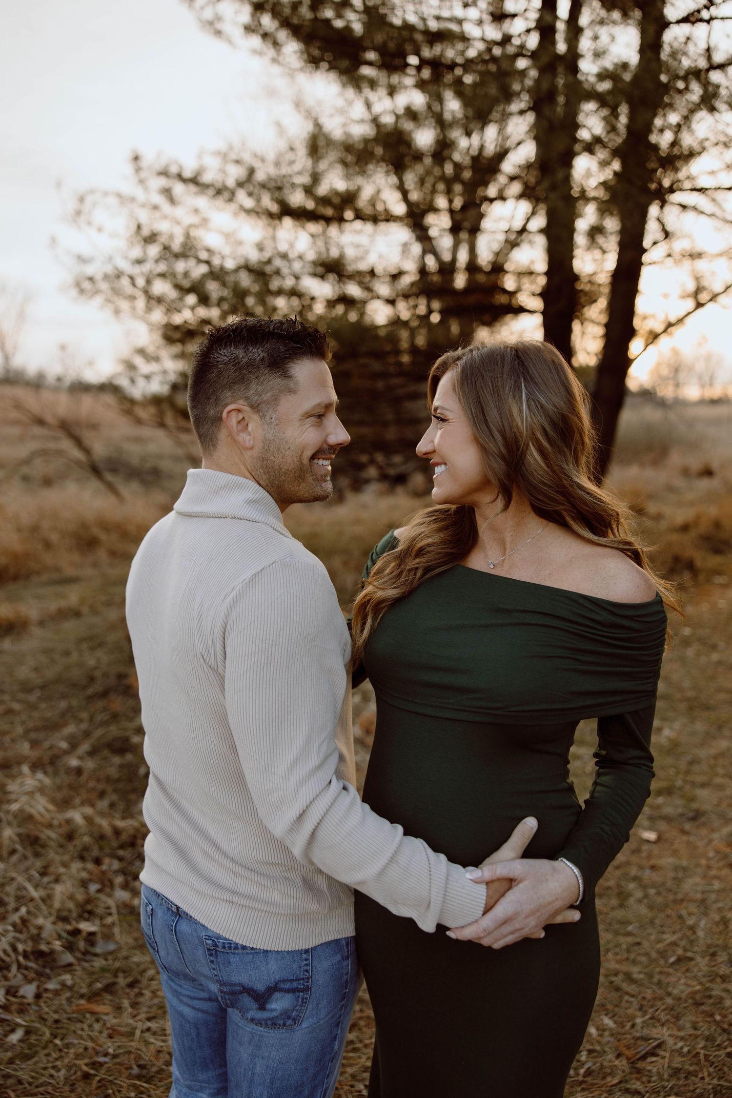Couple shares intimate moment during maternity photoshoot in wooded setting.