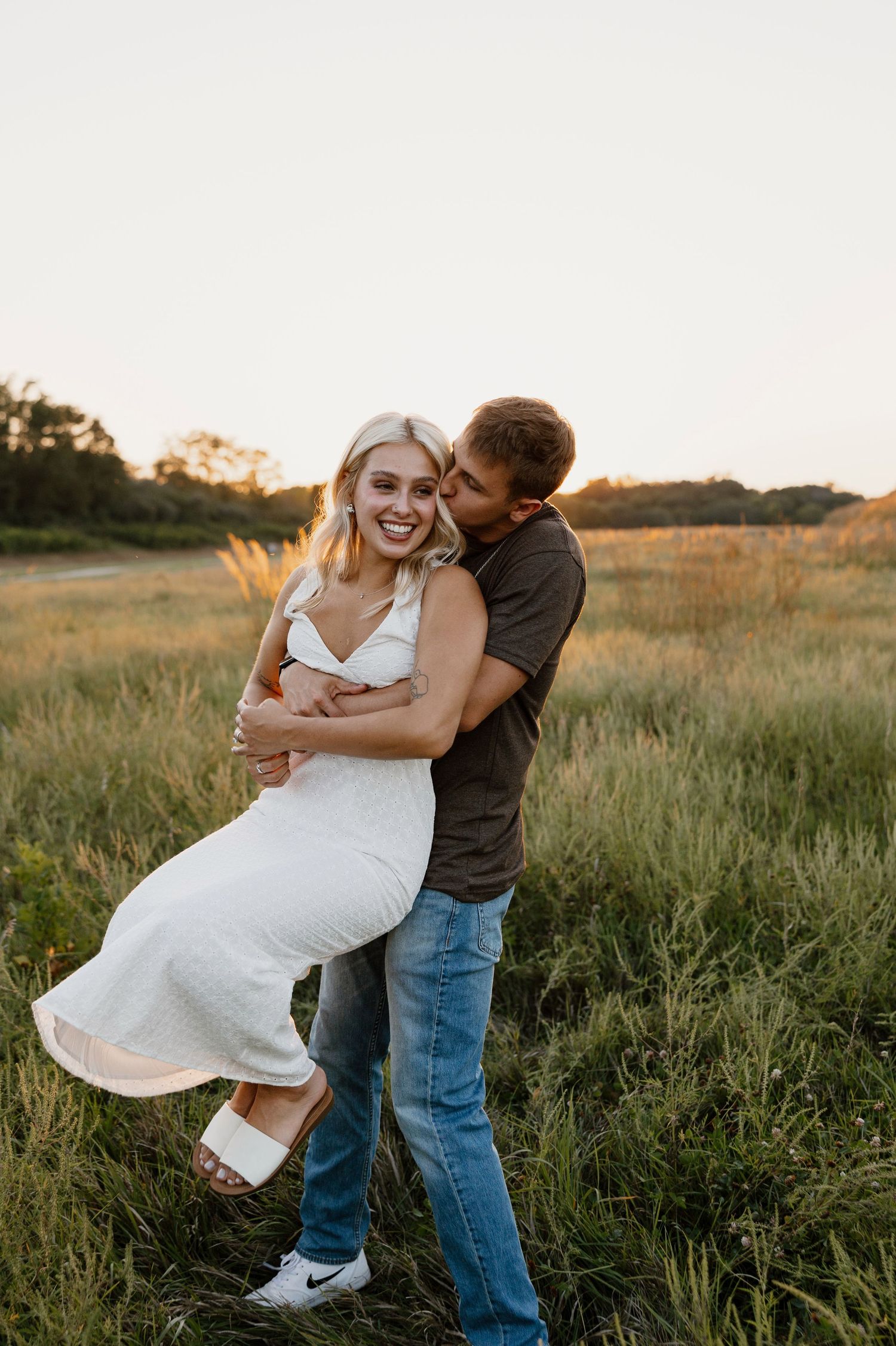 Romantic couple dancing in a golden field at sunset, with the woman wearing a white dress.