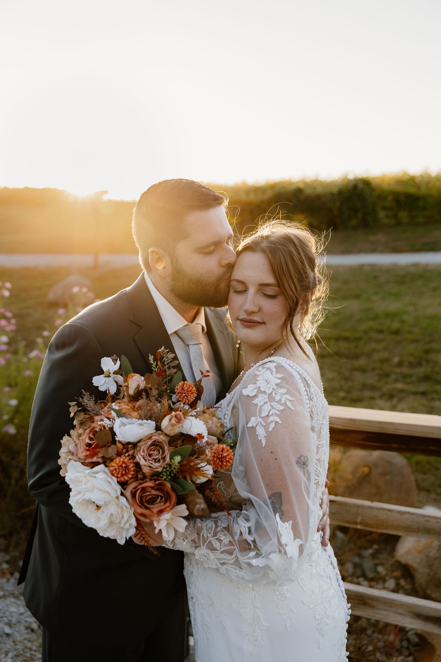 Newlyweds sharing intimate moment at sunset with autumn-colored bouquet.