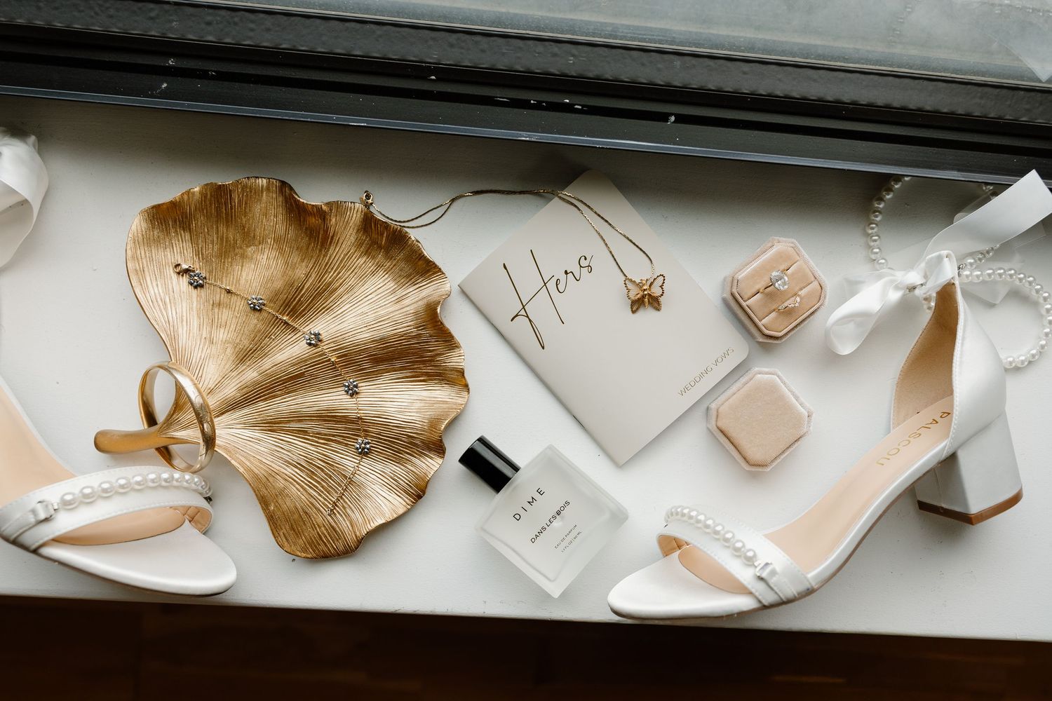 Wedding accessories flatlay with gold leaf, white shoes, and vows on paper.