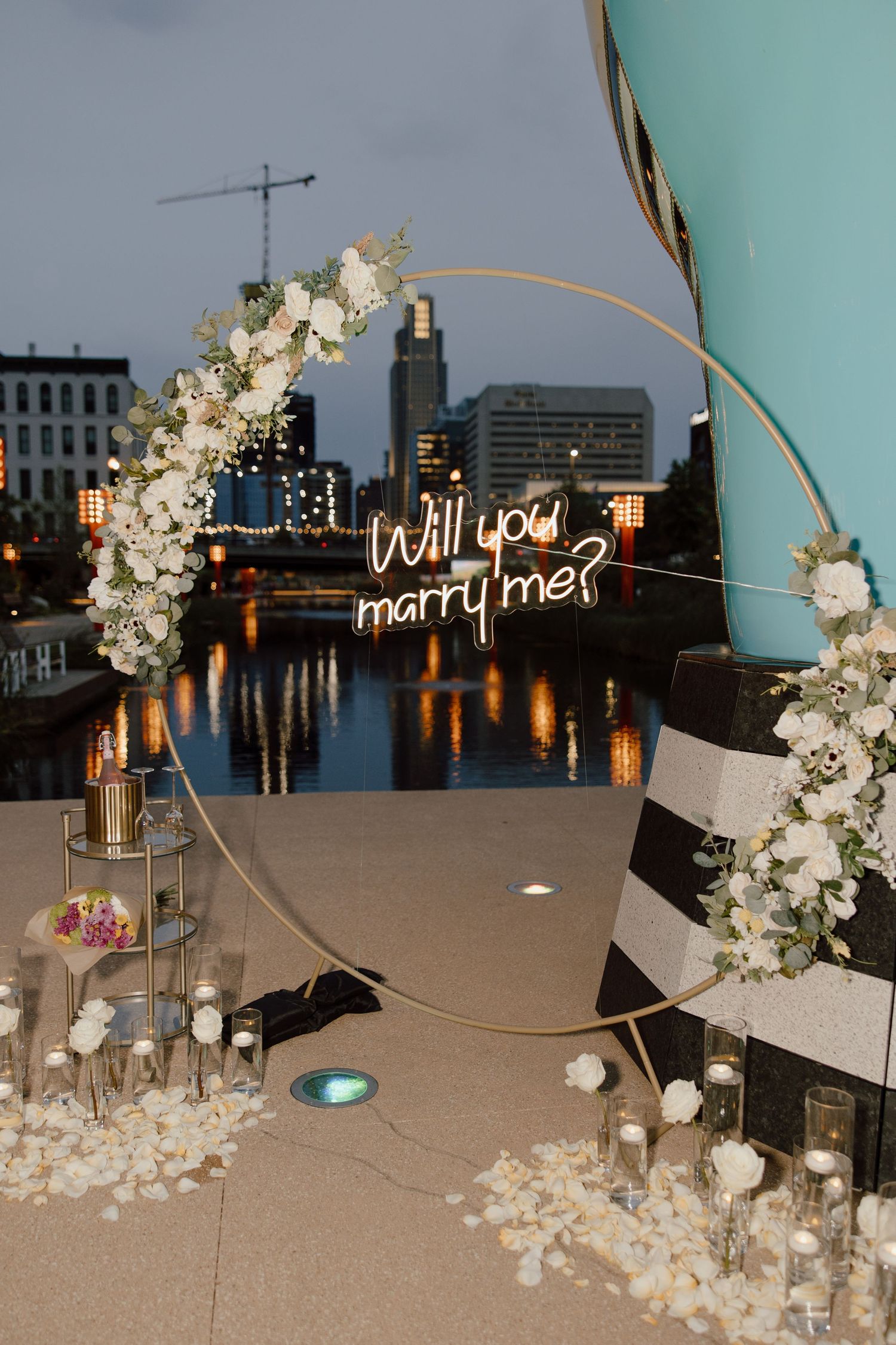 An illuminated neon sign reading 'Will you marry me?' with white floral decorations.