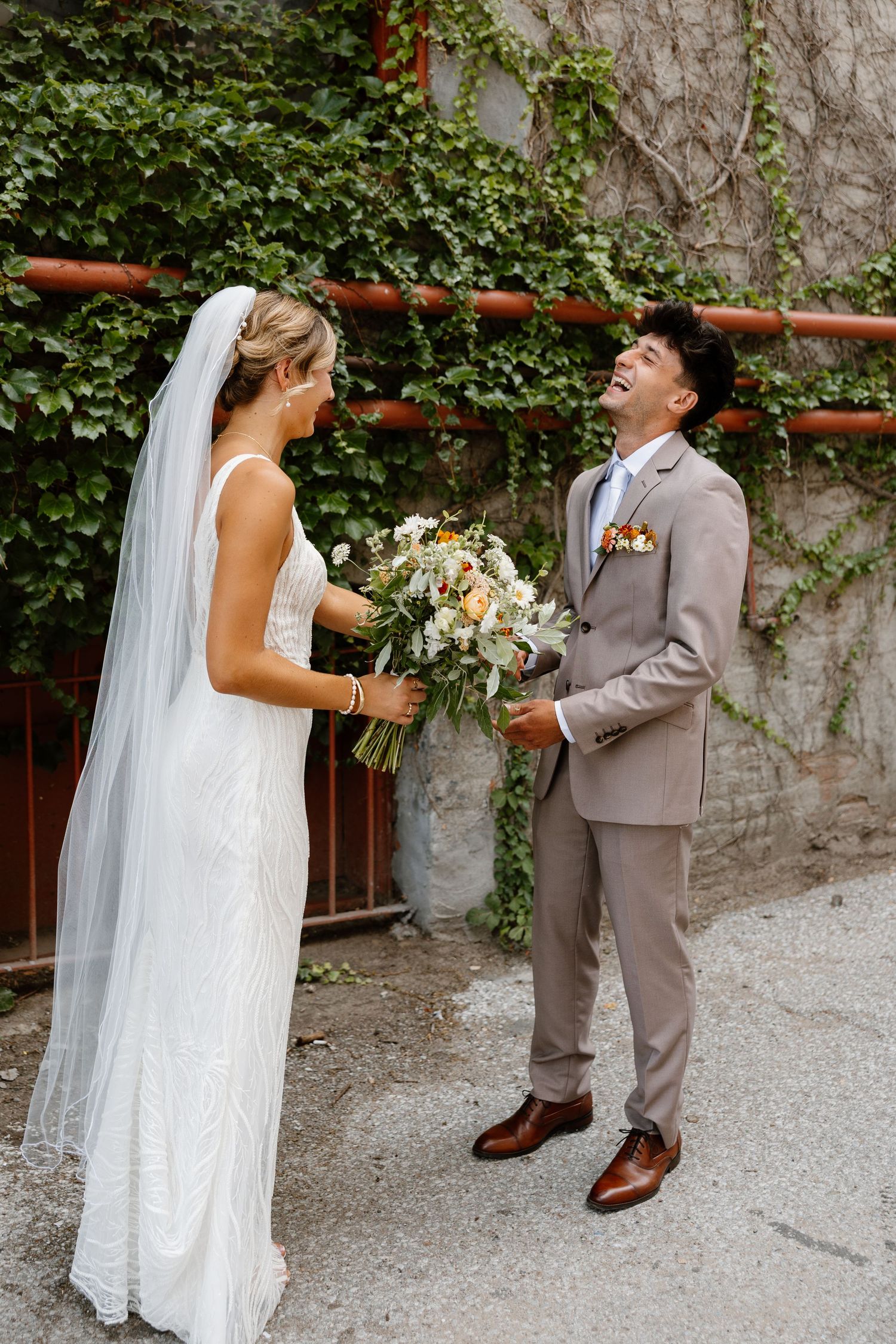Wedding couple in white dress and gray suit posing playfully outdoors.