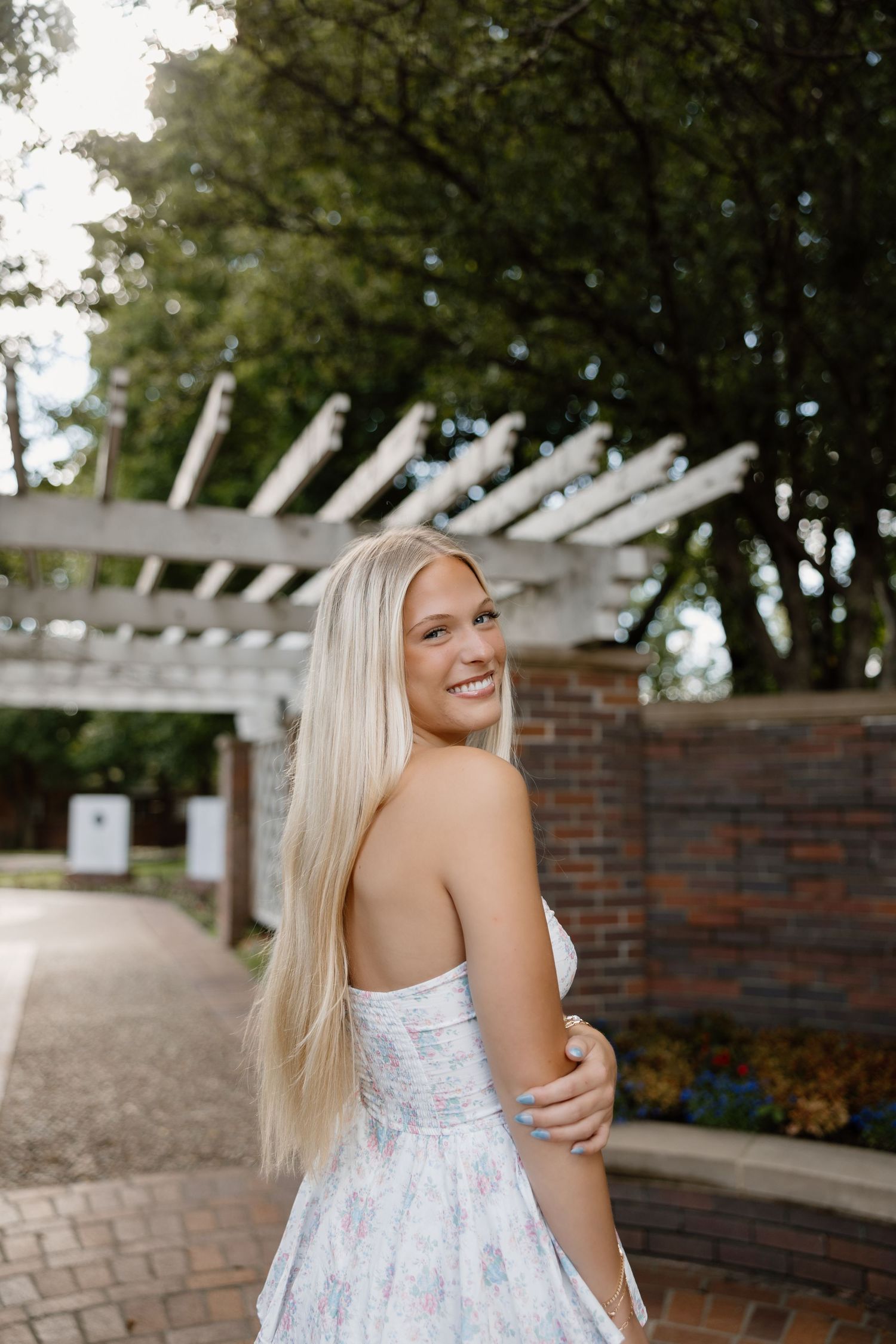 Summer portraits under pergola with brick wall and garden backdrop.