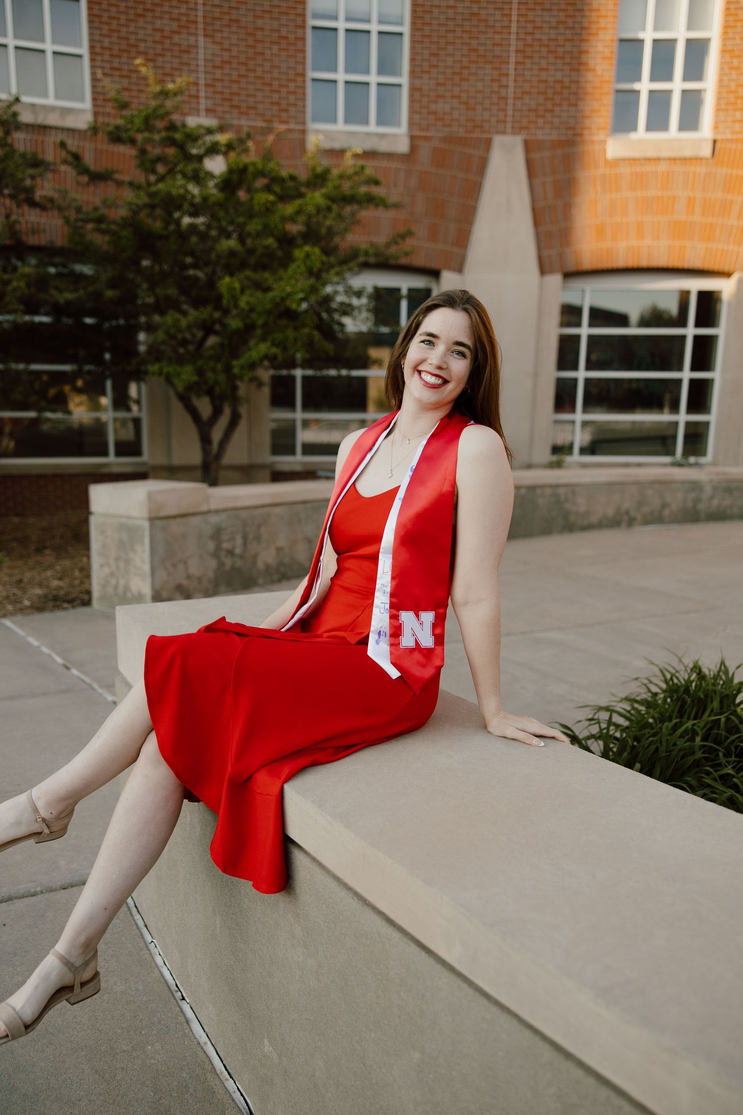 Graduate in bright red dress poses on concrete steps during graduation photoshoot.