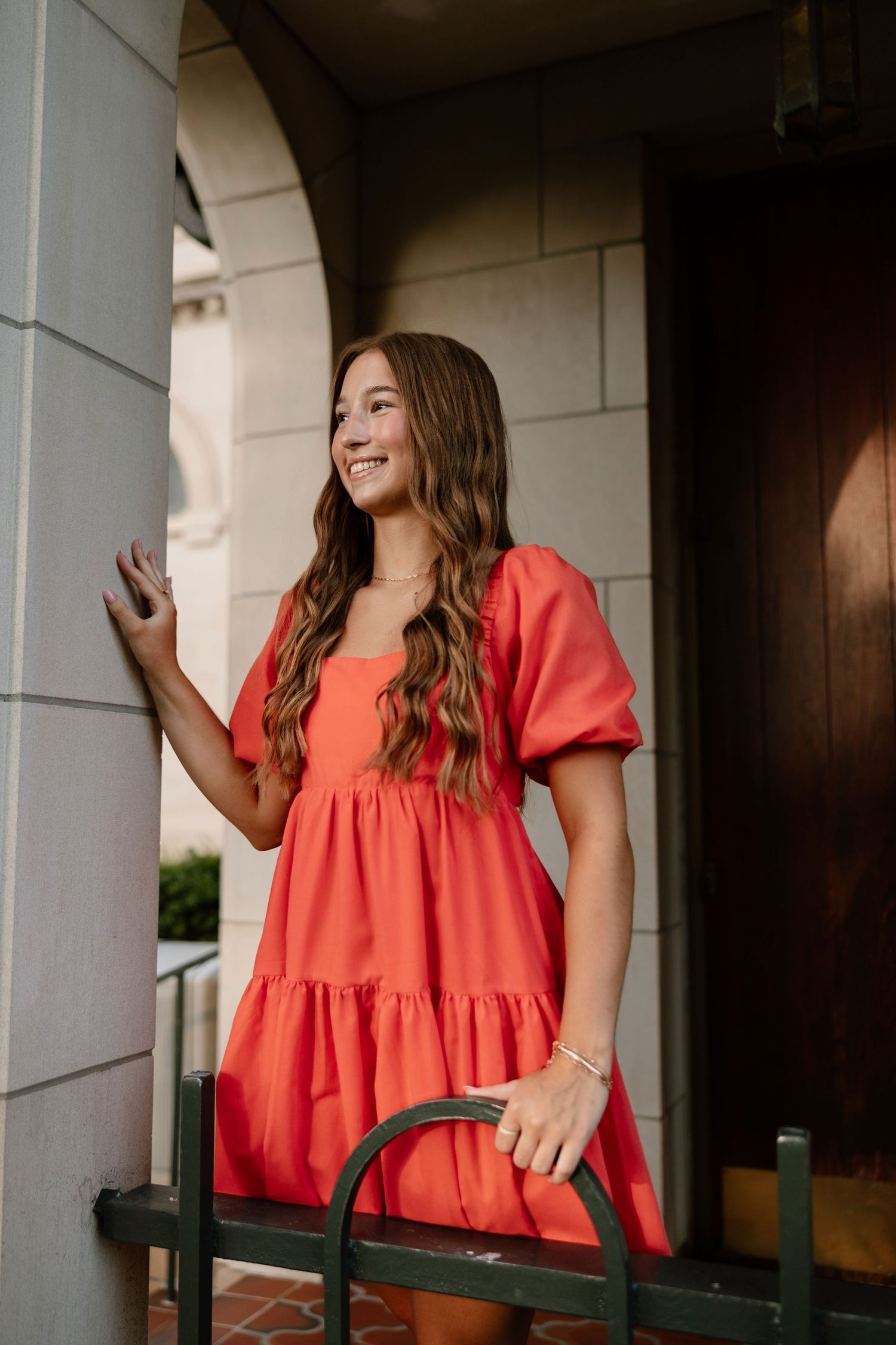 Portrait session under white architectural columns wearing a coral colored top.