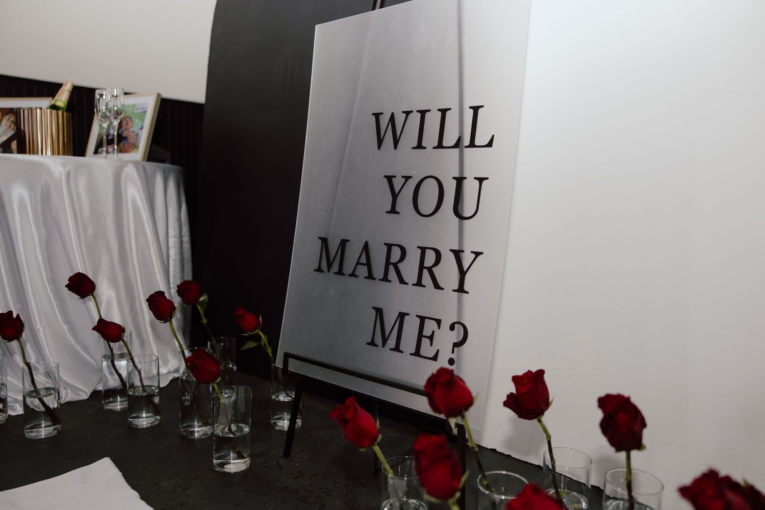 Empty room with 'WILL YOU MARRY ME?' text and red roses creating romantic proposal setting.