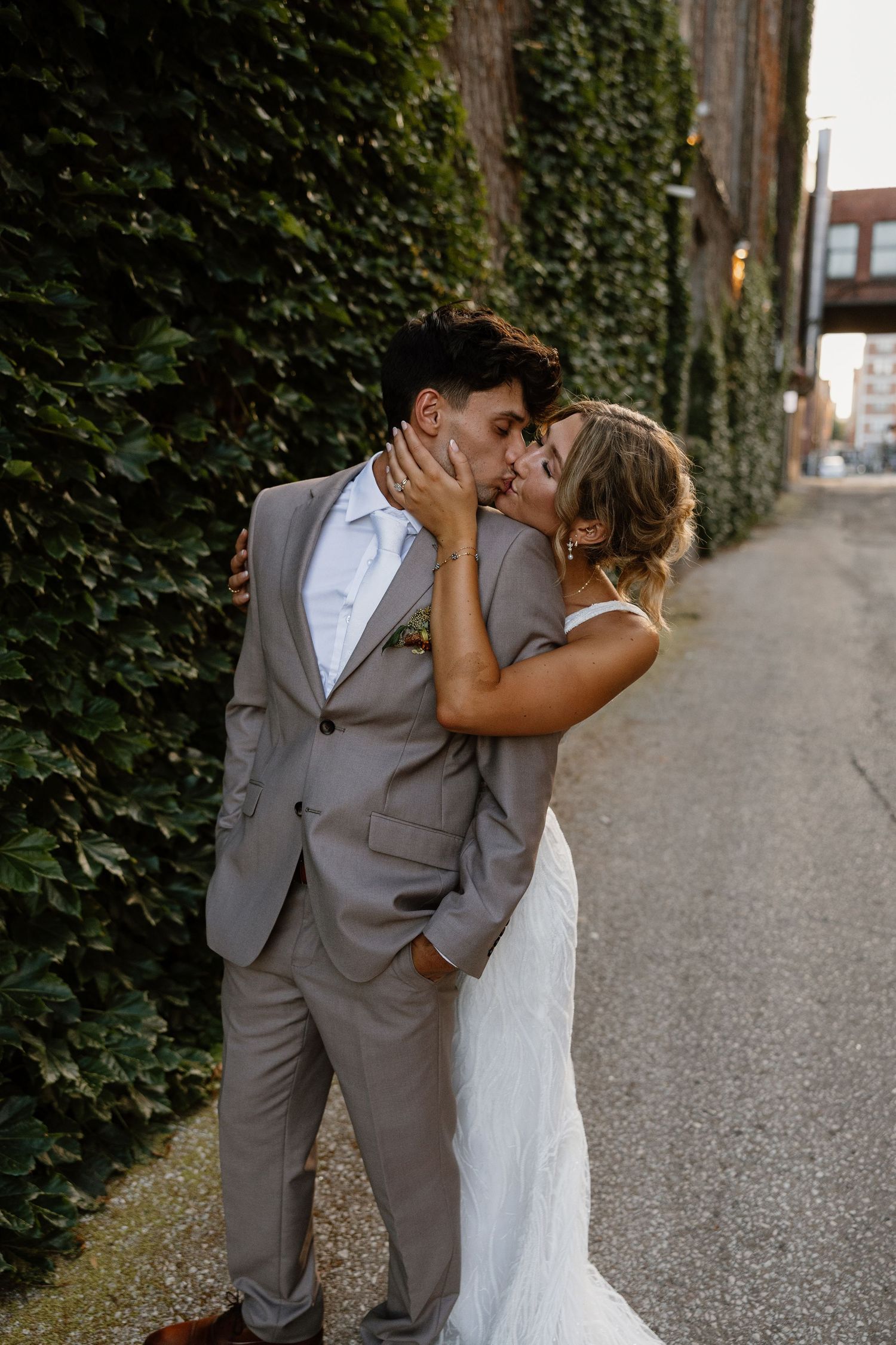 Couple in wedding attire shares intimate moments along an ivy-covered wall.