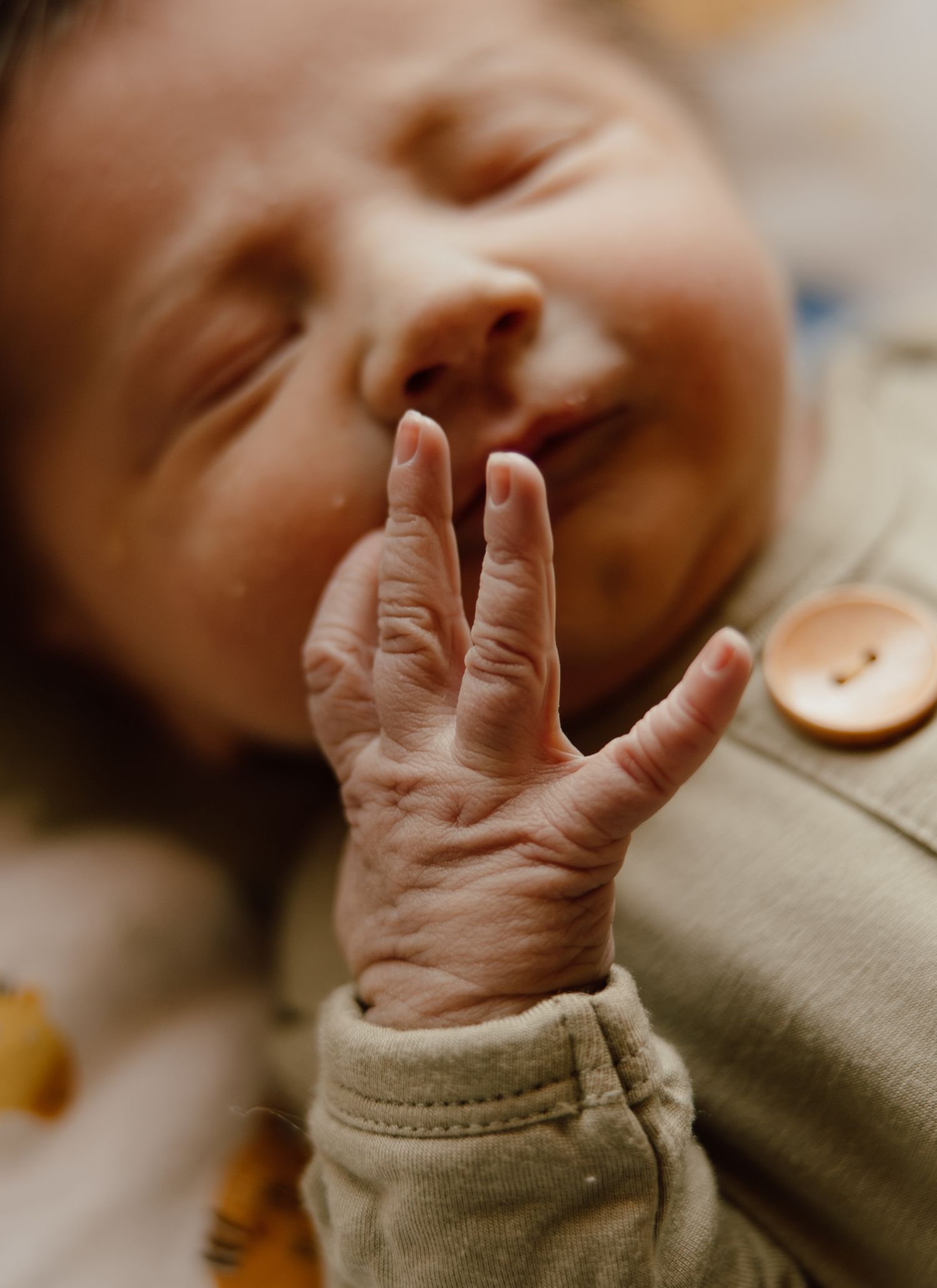 Close-up of tiny baby hand with delicate fingers against soft fabric.