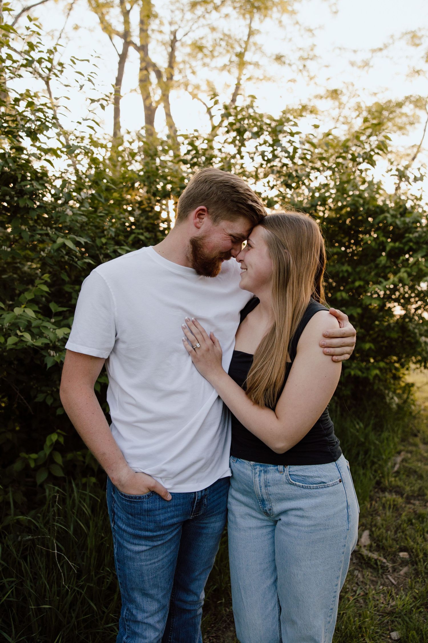 A couple embraces in a romantic moment against a natural backdrop at sunset.