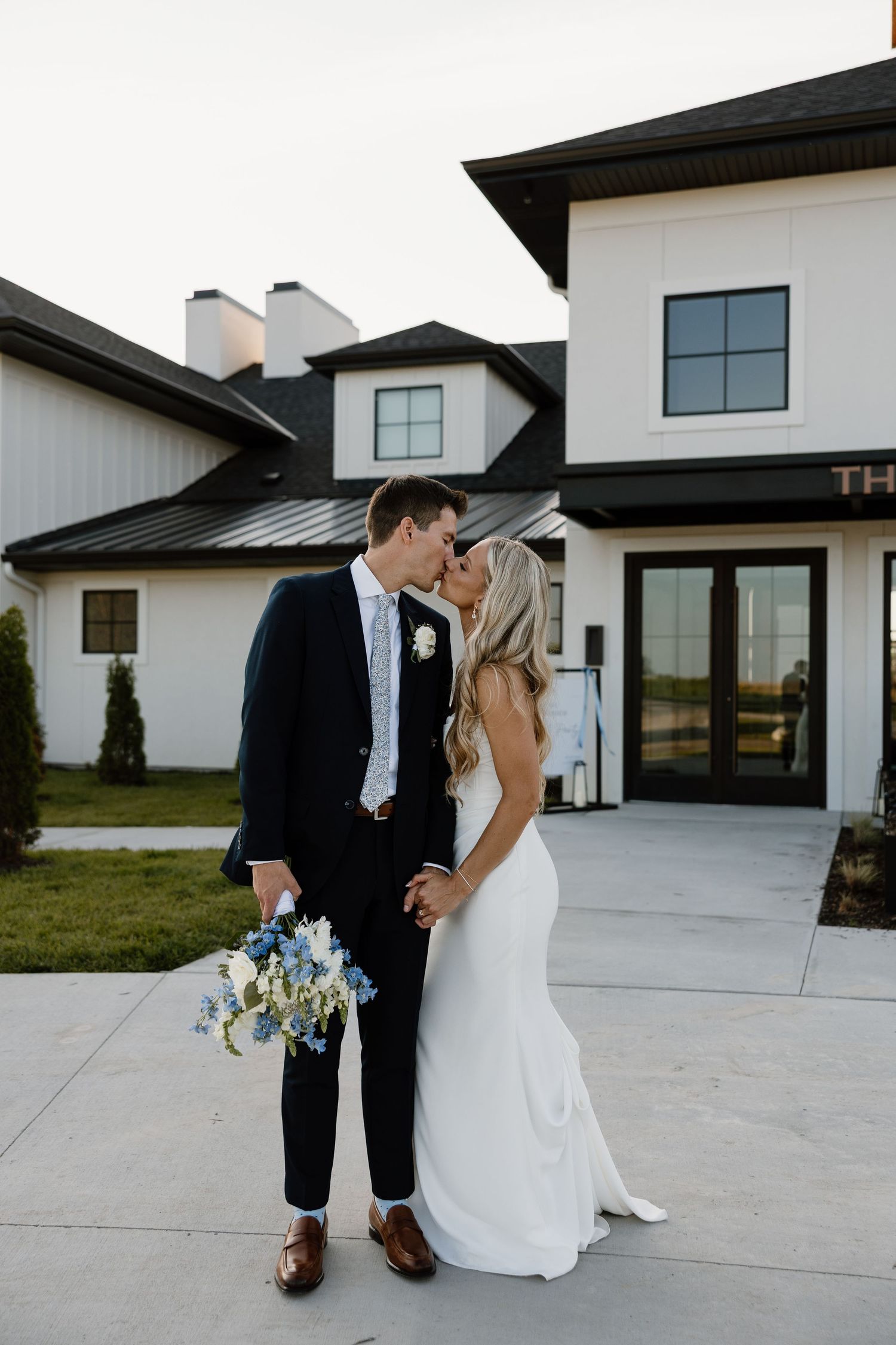 A bride and groom share a romantic moment outside a modern white farmhouse with black trim on their wedding day.