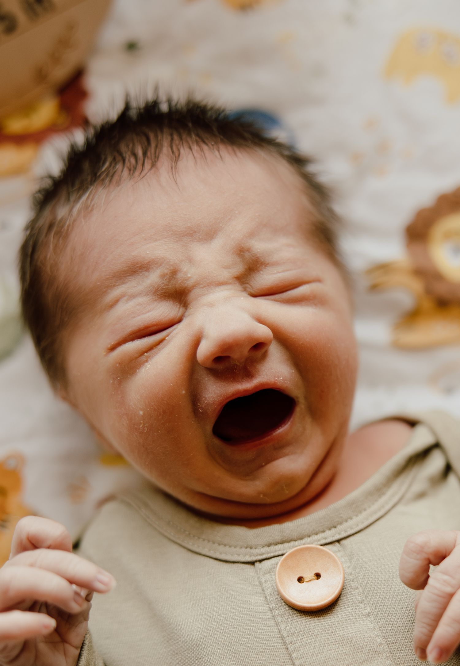 A joyful crying newborn baby wearing a beige outfit with a decorative button.