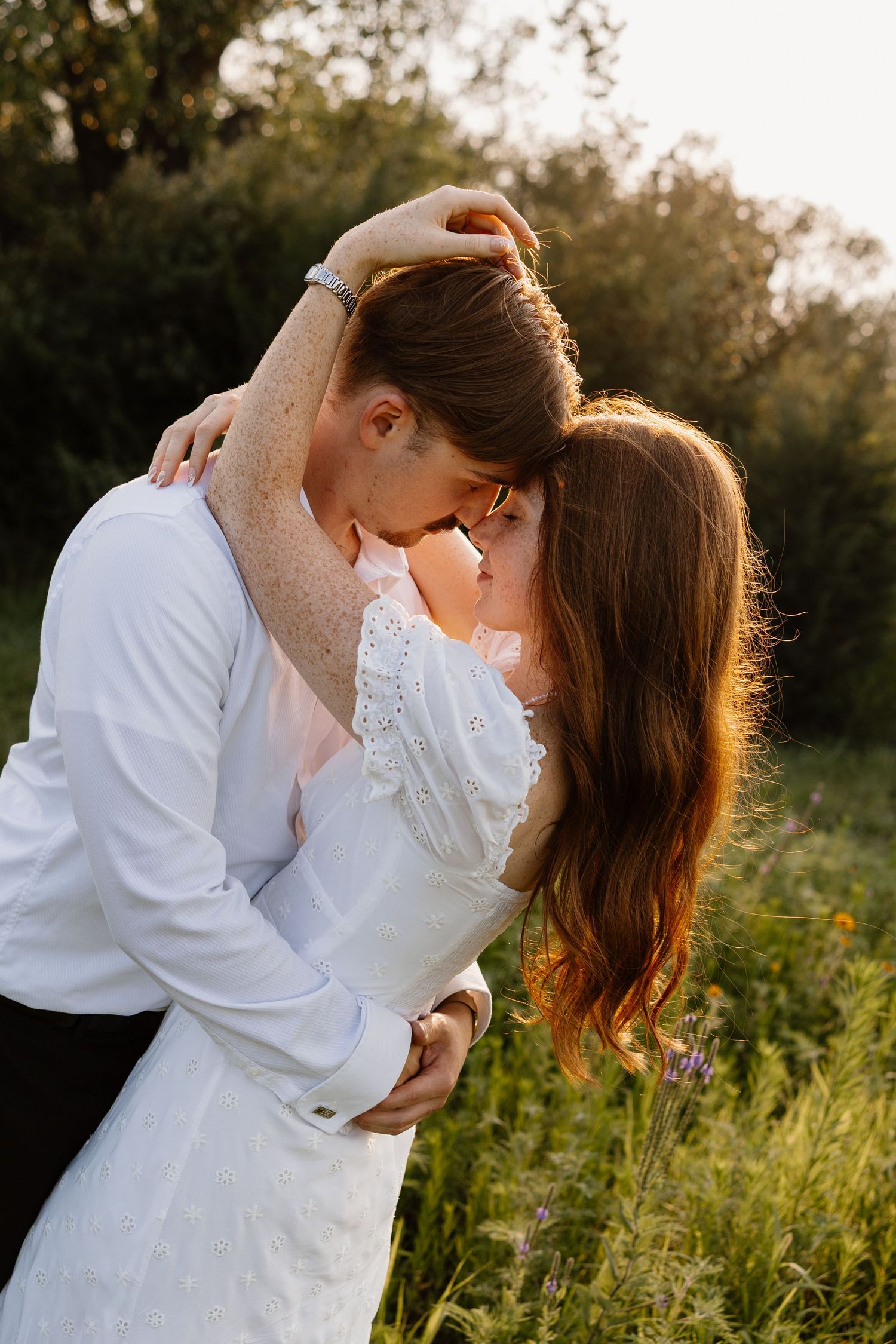 A romantic sunset portrait of a couple embracing in a field with golden backlighting.