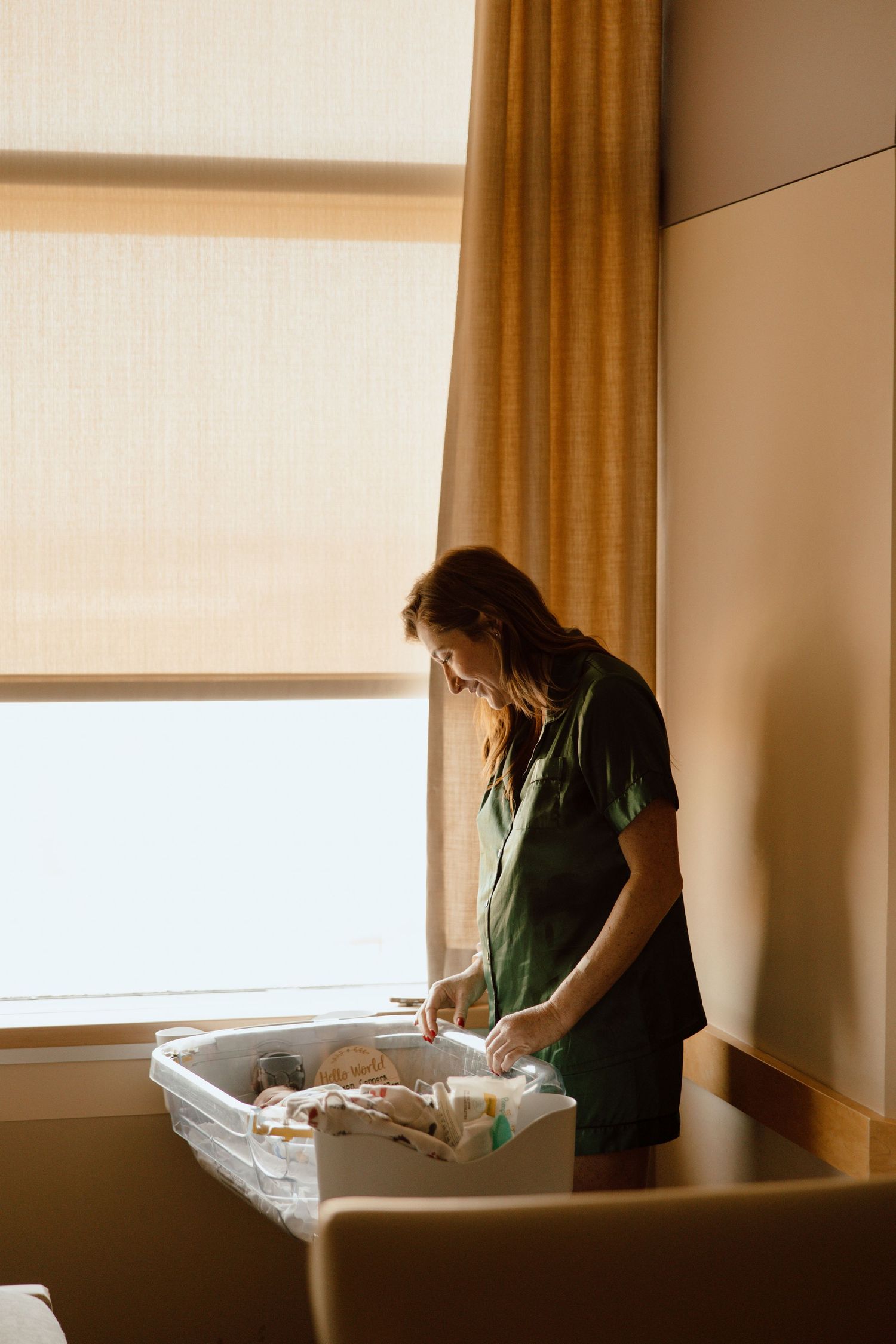 Silhouette of person tending to bassinet near sunlit window.