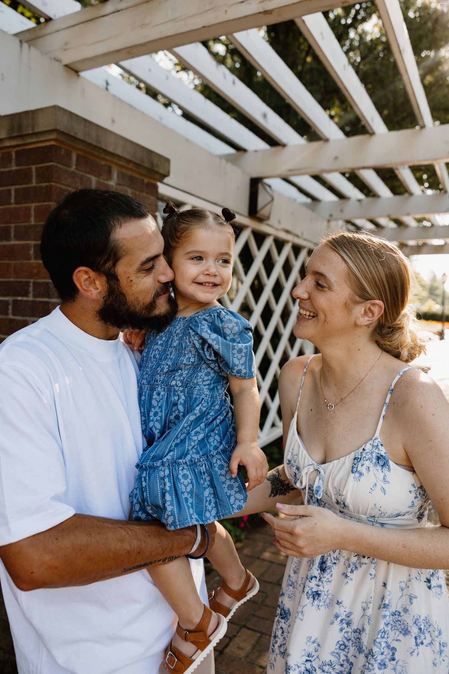 Family shares joyful moments under a white pergola wearing coordinated blue and white outfits.