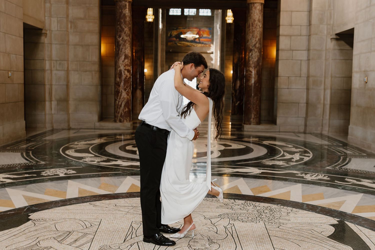 Romantic dance poses captured in grand historic building interior with patterned floor.