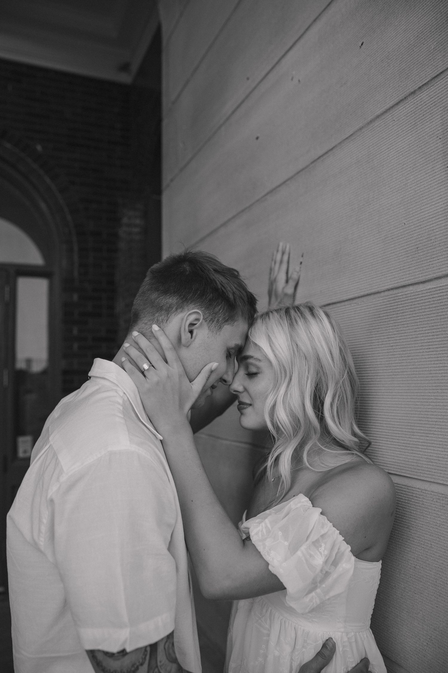 A black and white intimate portrait of a couple against a textured wall.