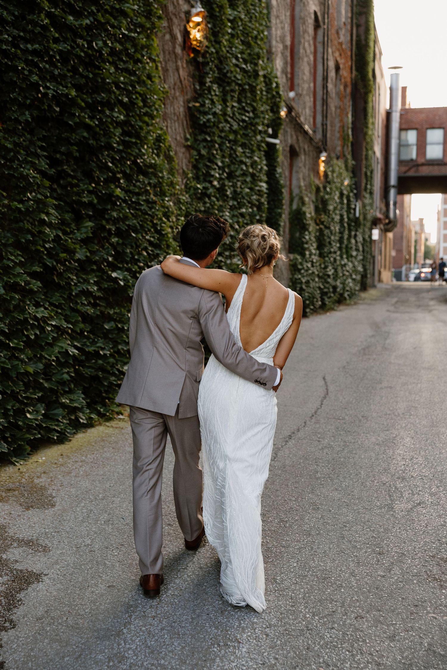 Newlyweds walk hand in hand down ivy-lined alley on their wedding day.