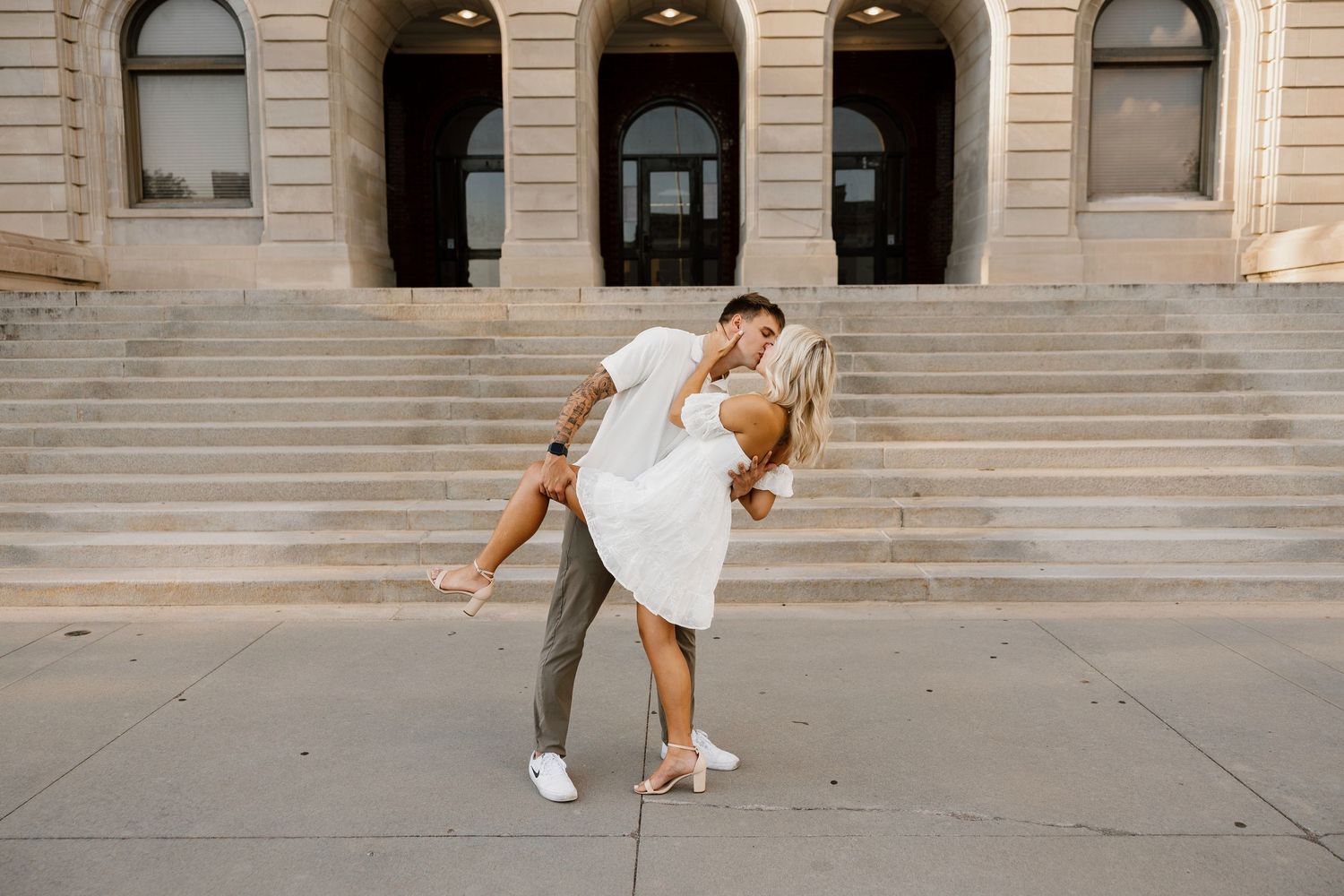 A couple strolls playfully across a stone courtyard in front of a classical building.