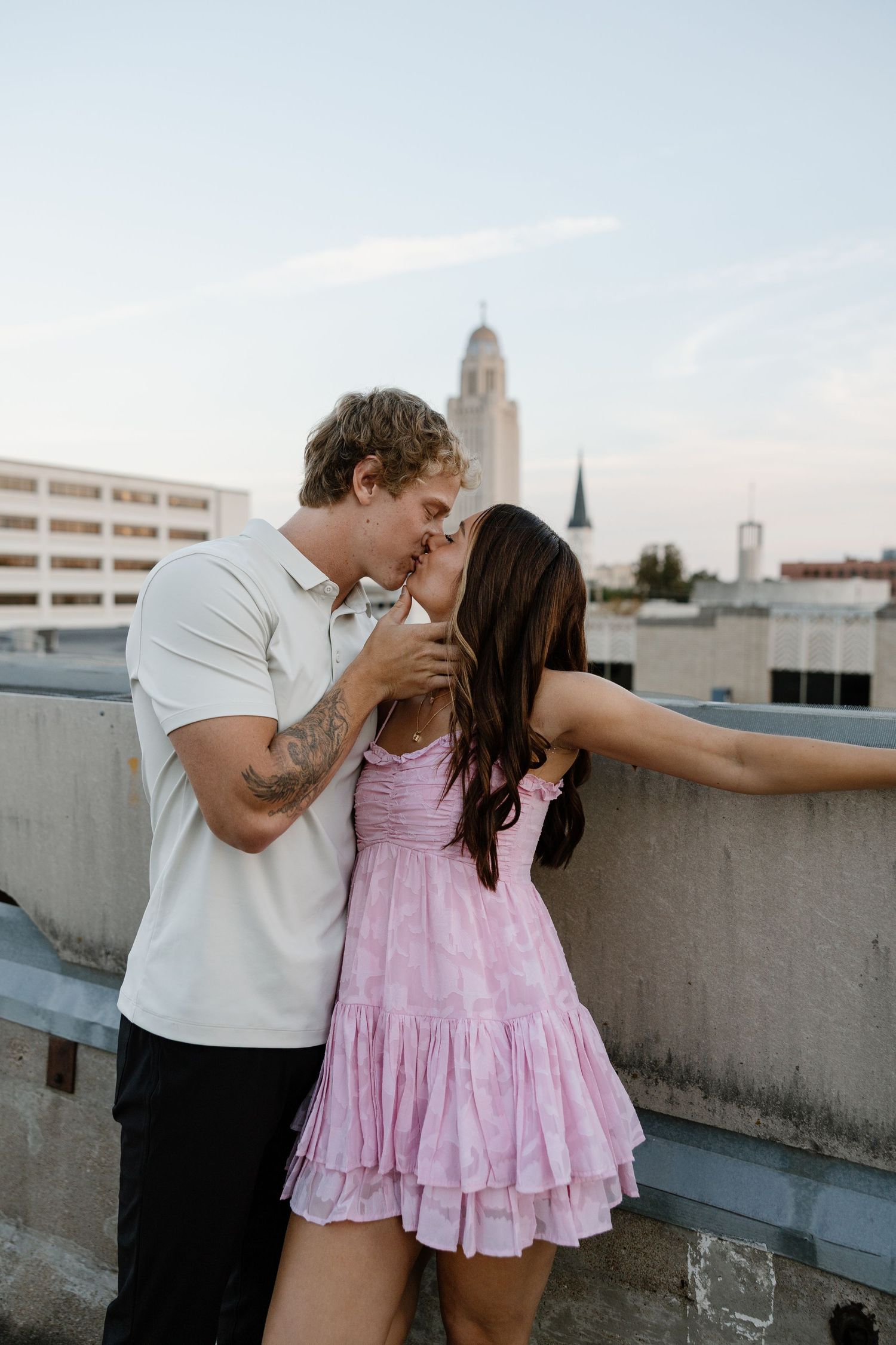 A couple shares a romantic moment on an urban rooftop with city buildings in the background.