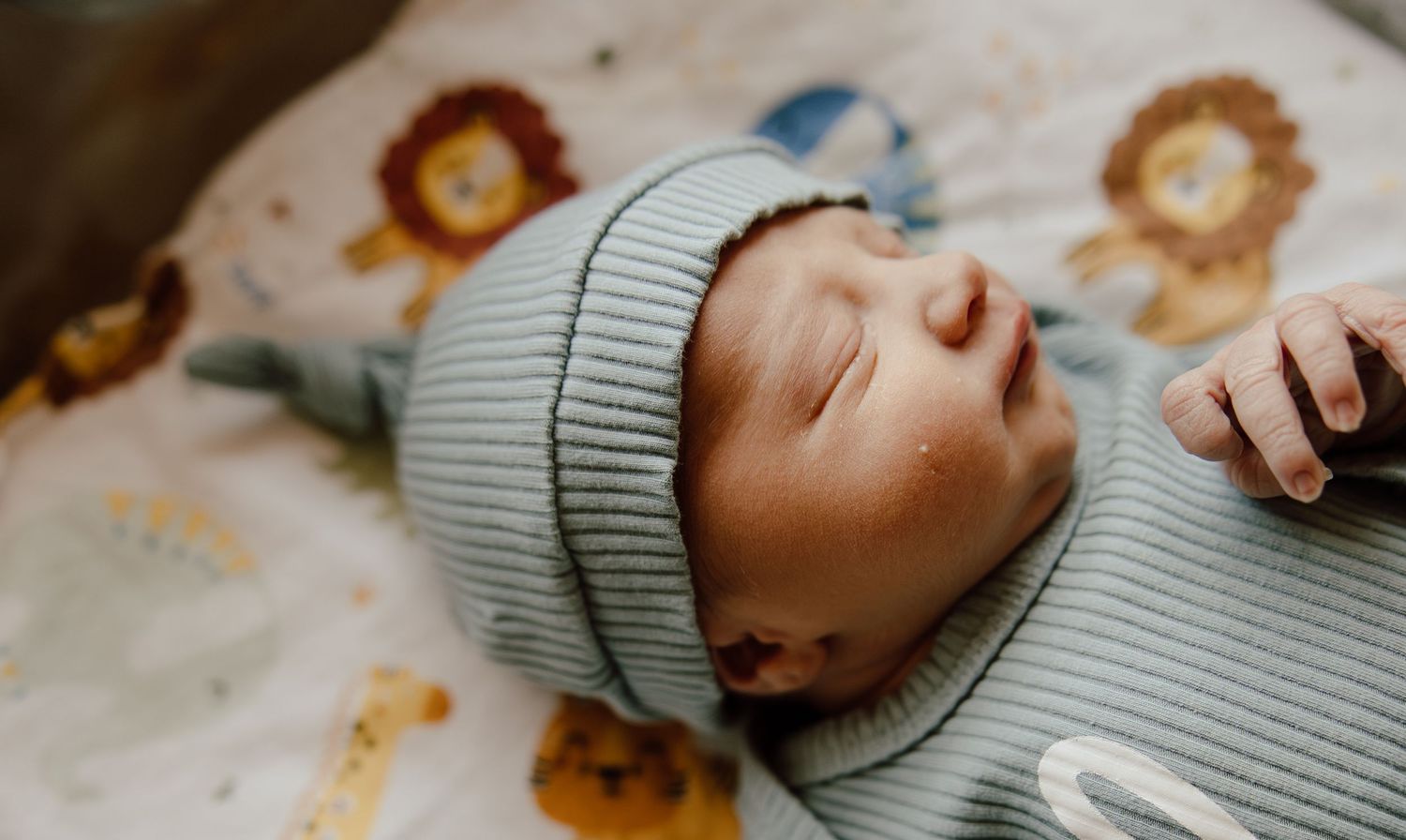 Newborn baby wearing a soft mint green ribbed outfit lies on patterned bedding.