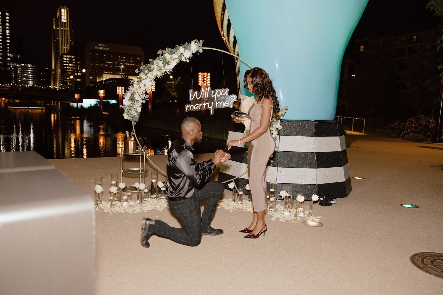 A nighttime proposal scene on a rooftop with decorative lighting and flowers.