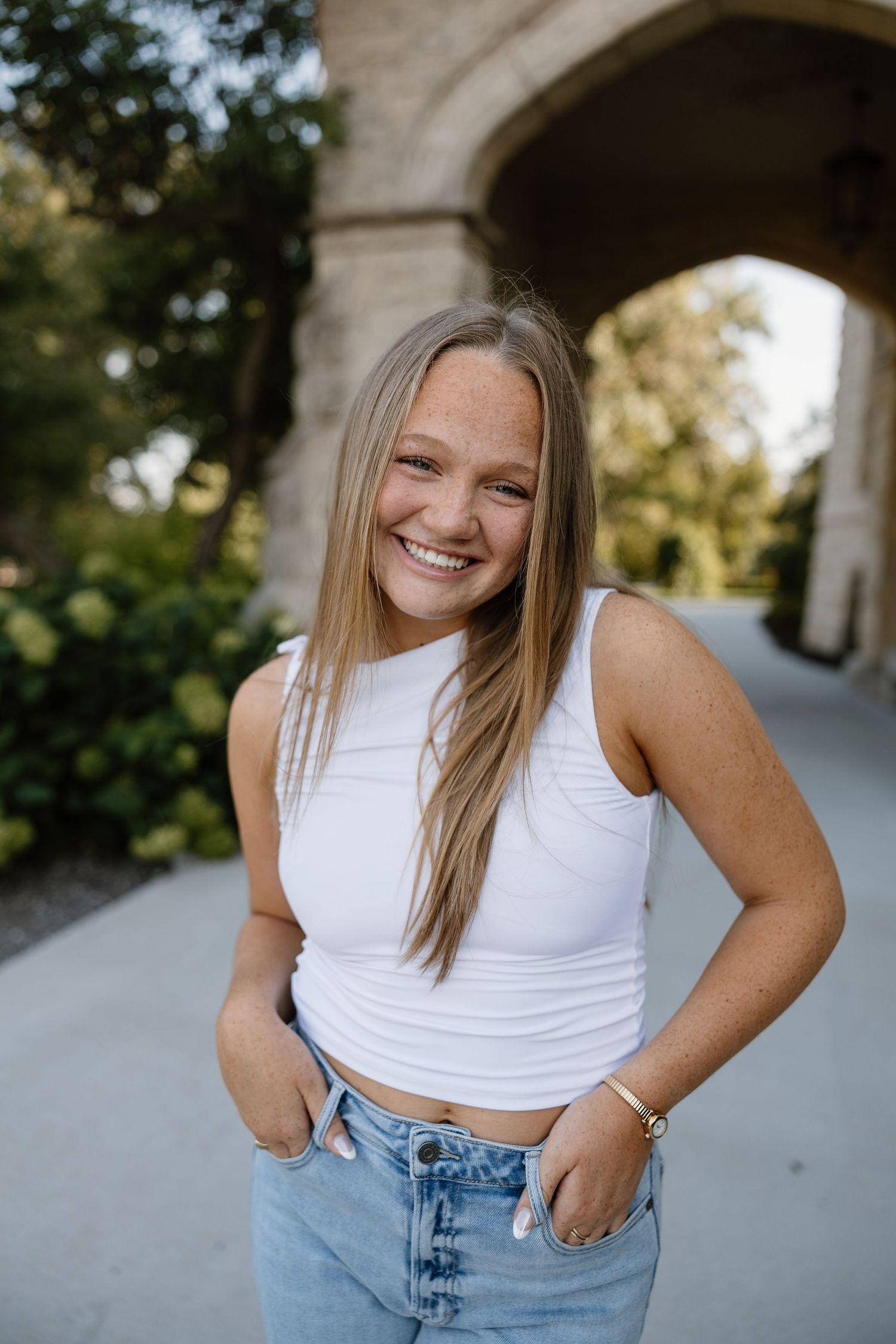Portrait series in front of stone archway with white crop top and jeans.