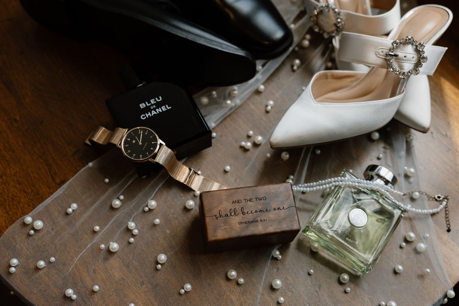 Wedding accessories and details arranged on dark wooden surface with scattered pearls.