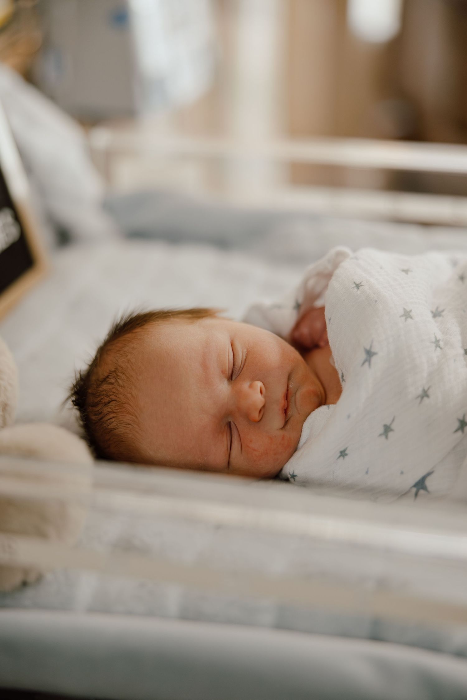 Sleeping newborn baby wrapped in a star-patterned swaddle blanket rests peacefully.