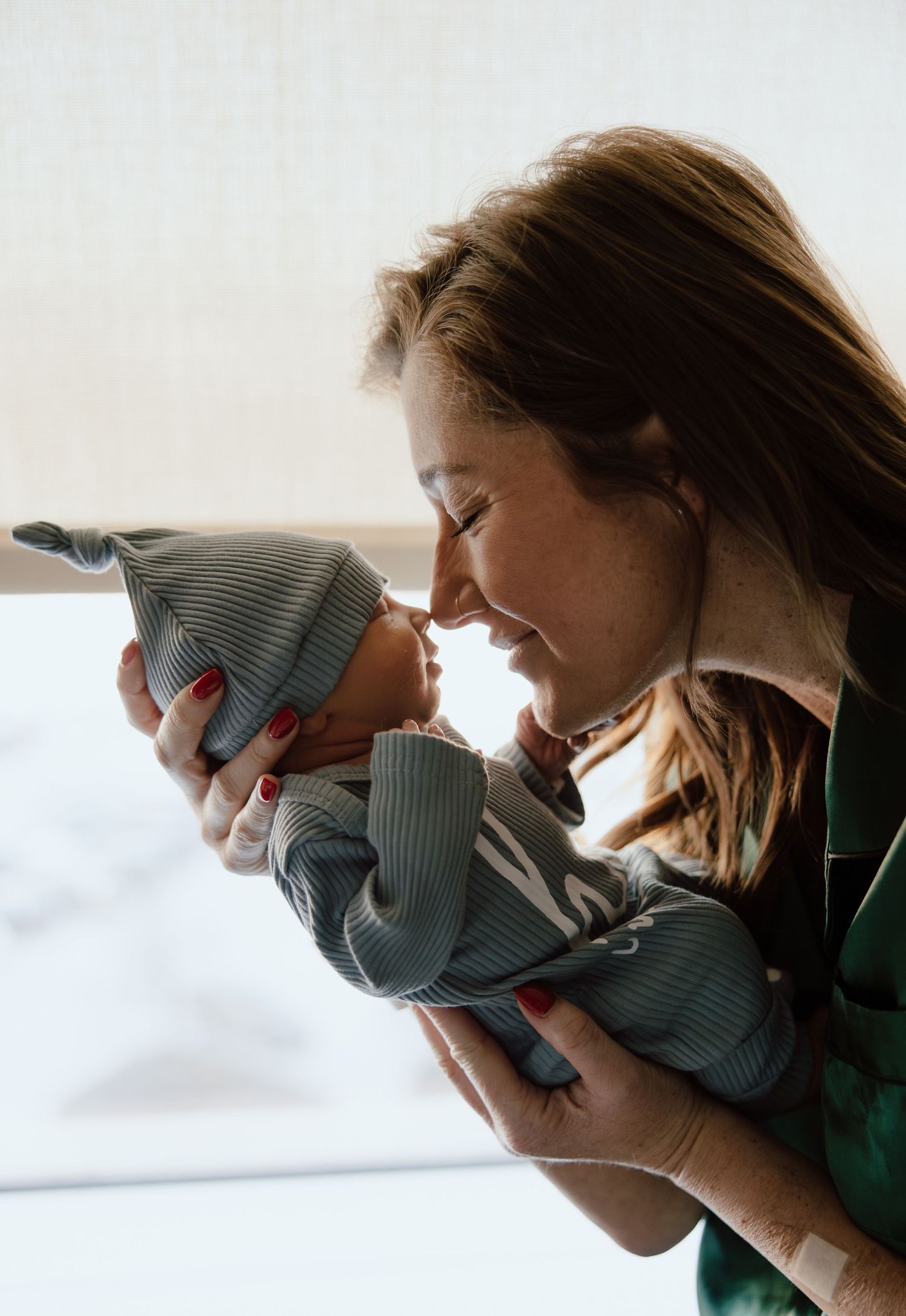 A tender moment between parent and baby in gray knit clothing by a window with soft natural light.