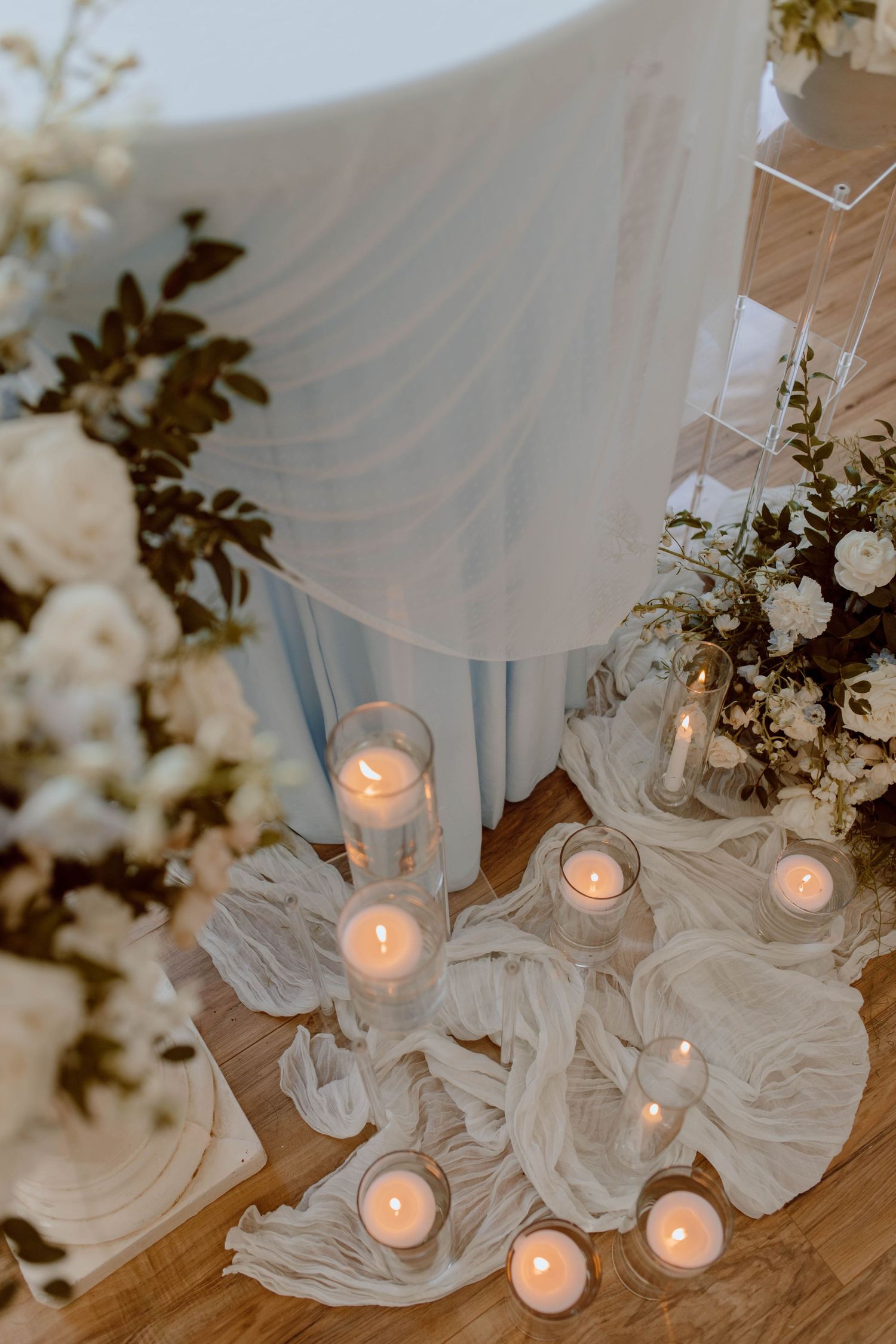 Glowing tea light candles nestled in flowing white fabric create a romantic atmosphere with floral arrangements nearby.