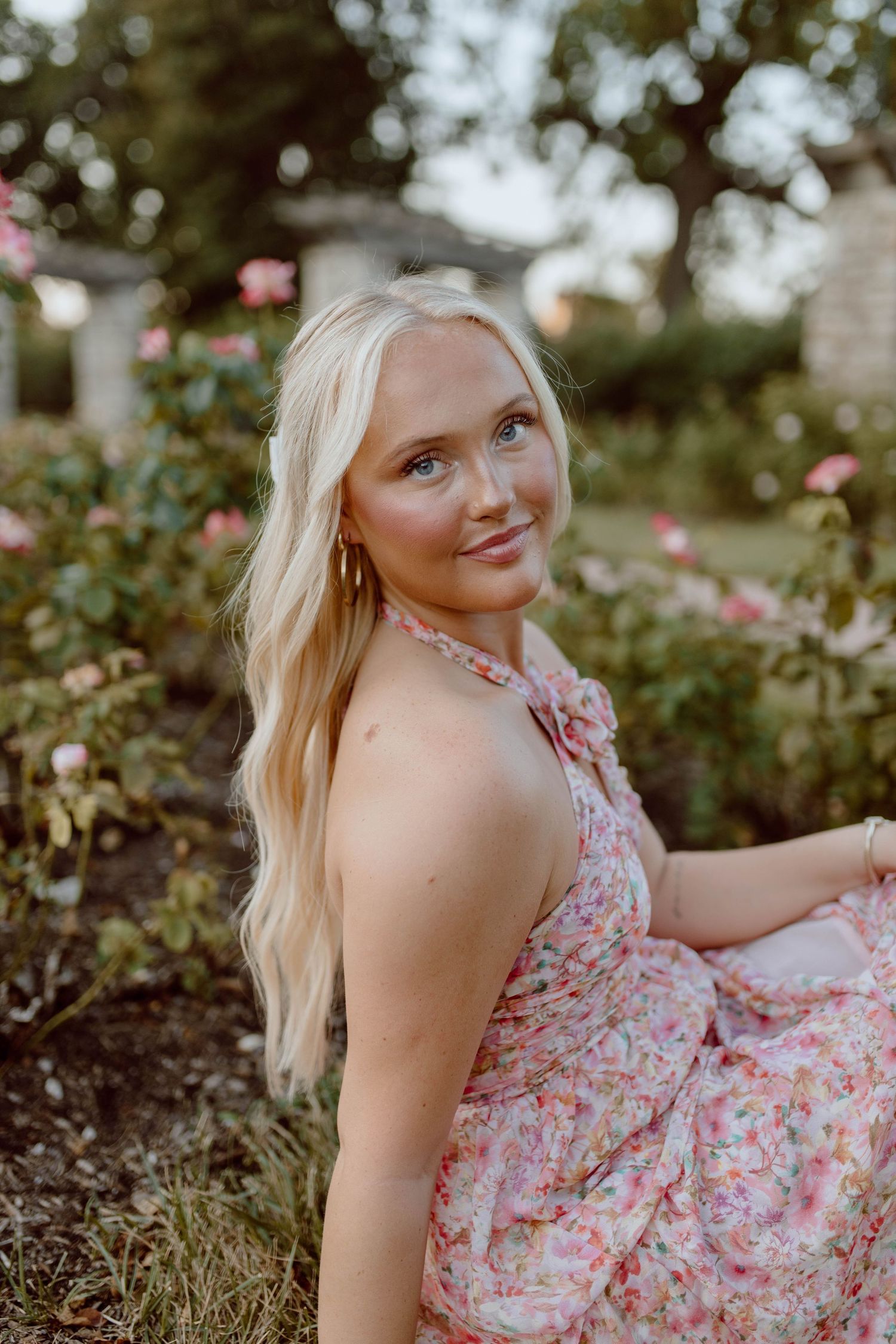 A portrait in a garden with pink roses featuring a floral dress and long blonde hair.