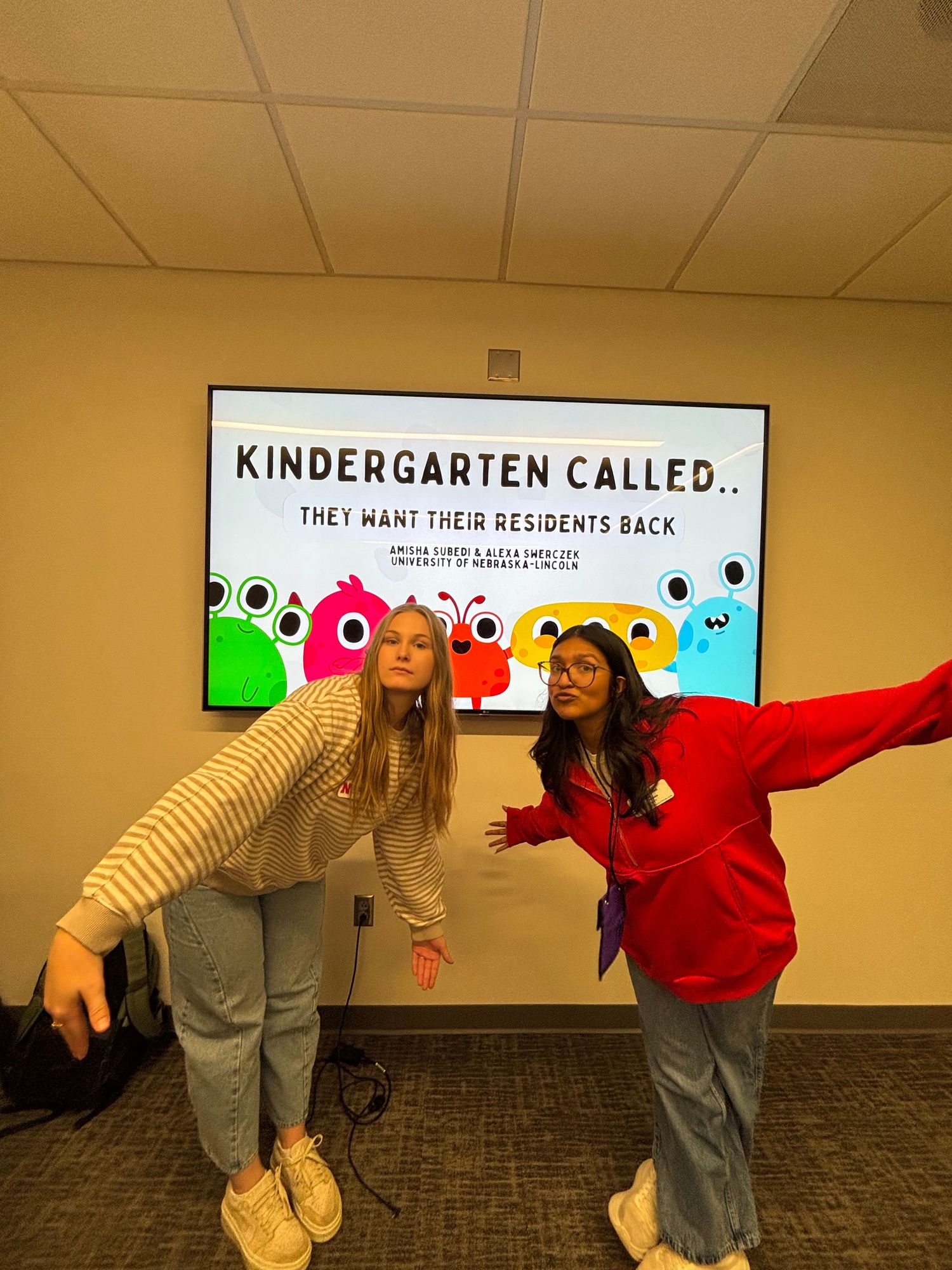 Two students pose in front of a presentation screen reading Kindergarten Called They Want Their Residents Back.