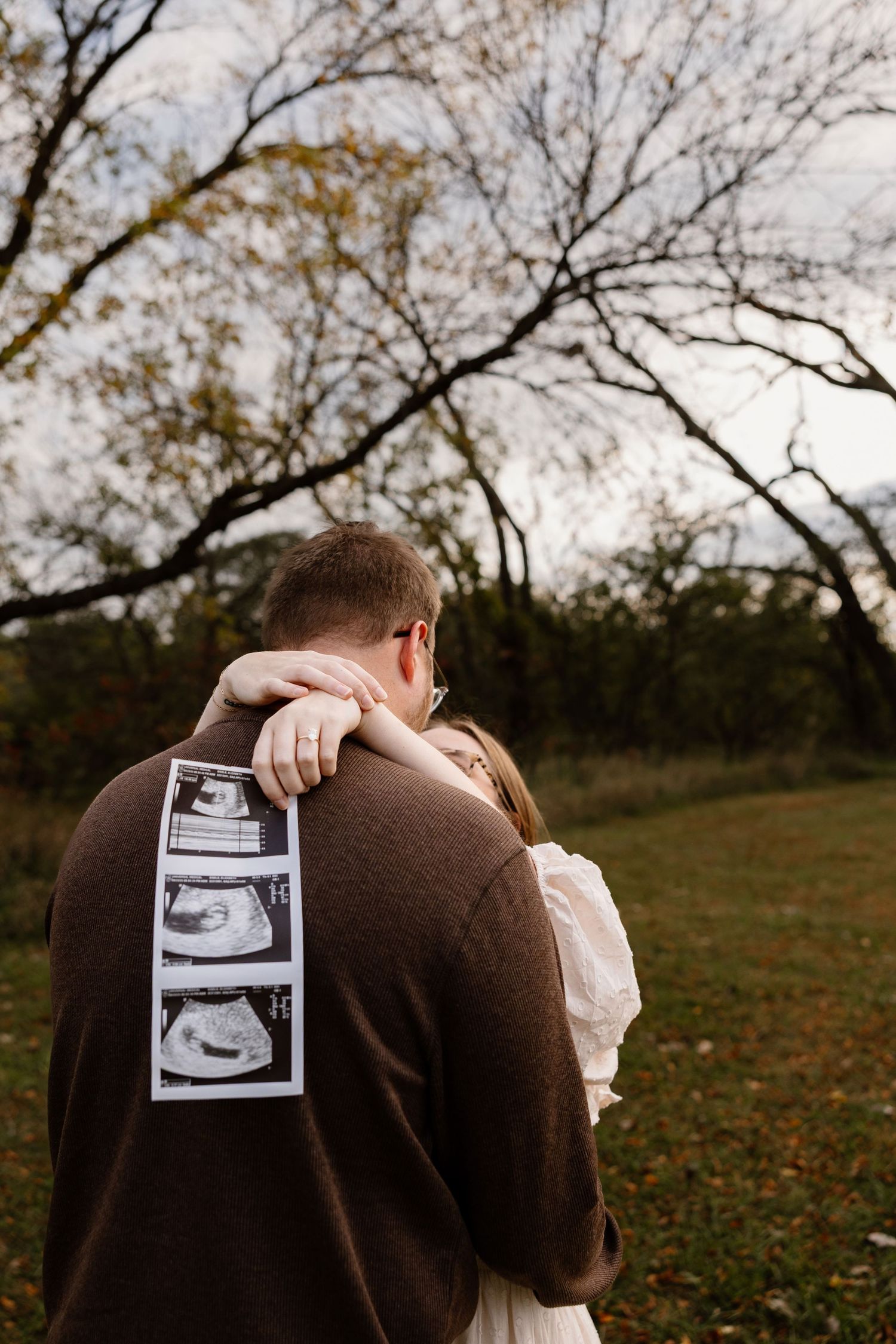 Couple embracing while holding ultrasound photos in autumn setting.