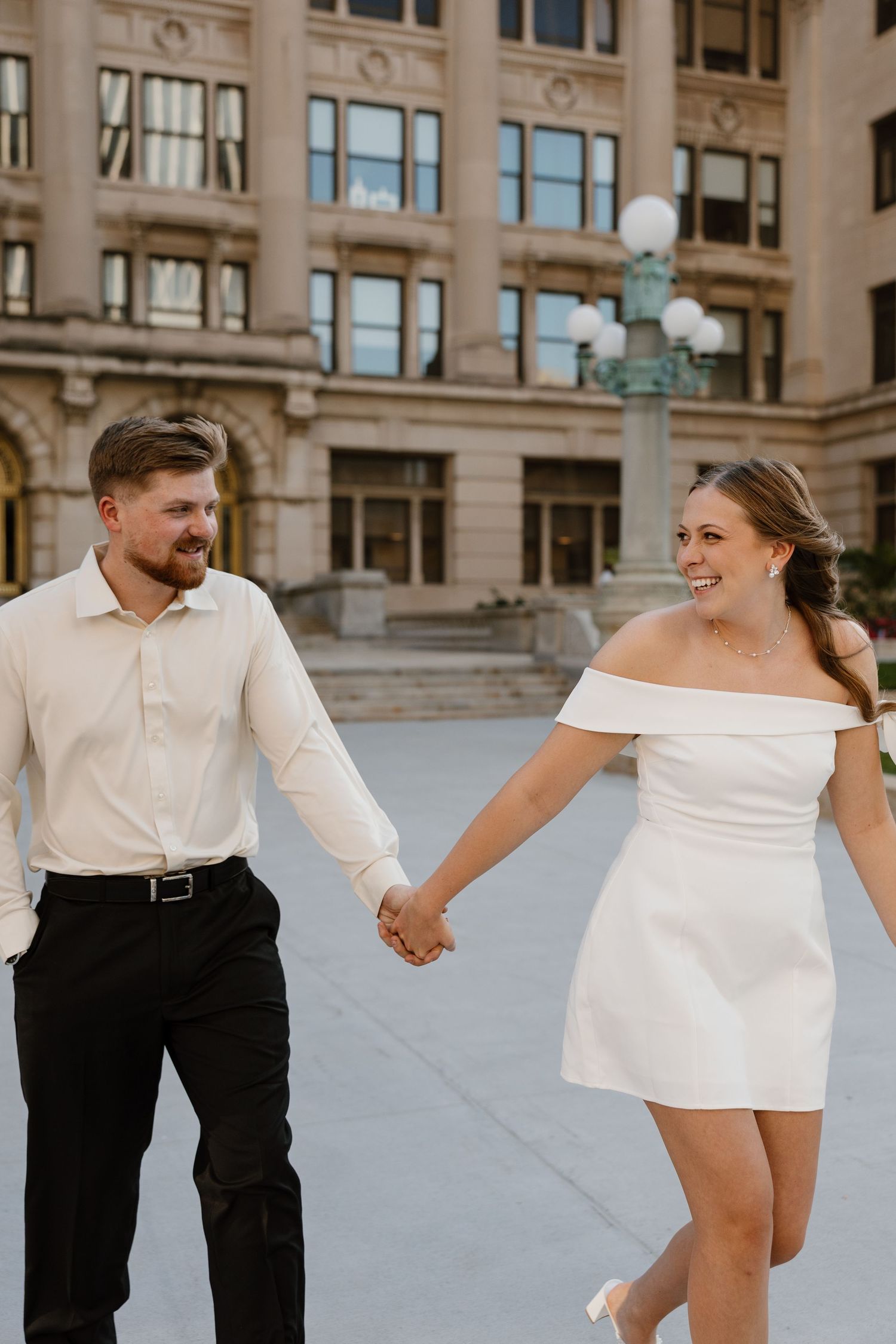 Couple dances and twirls together on plaza with elegant building facade in background.