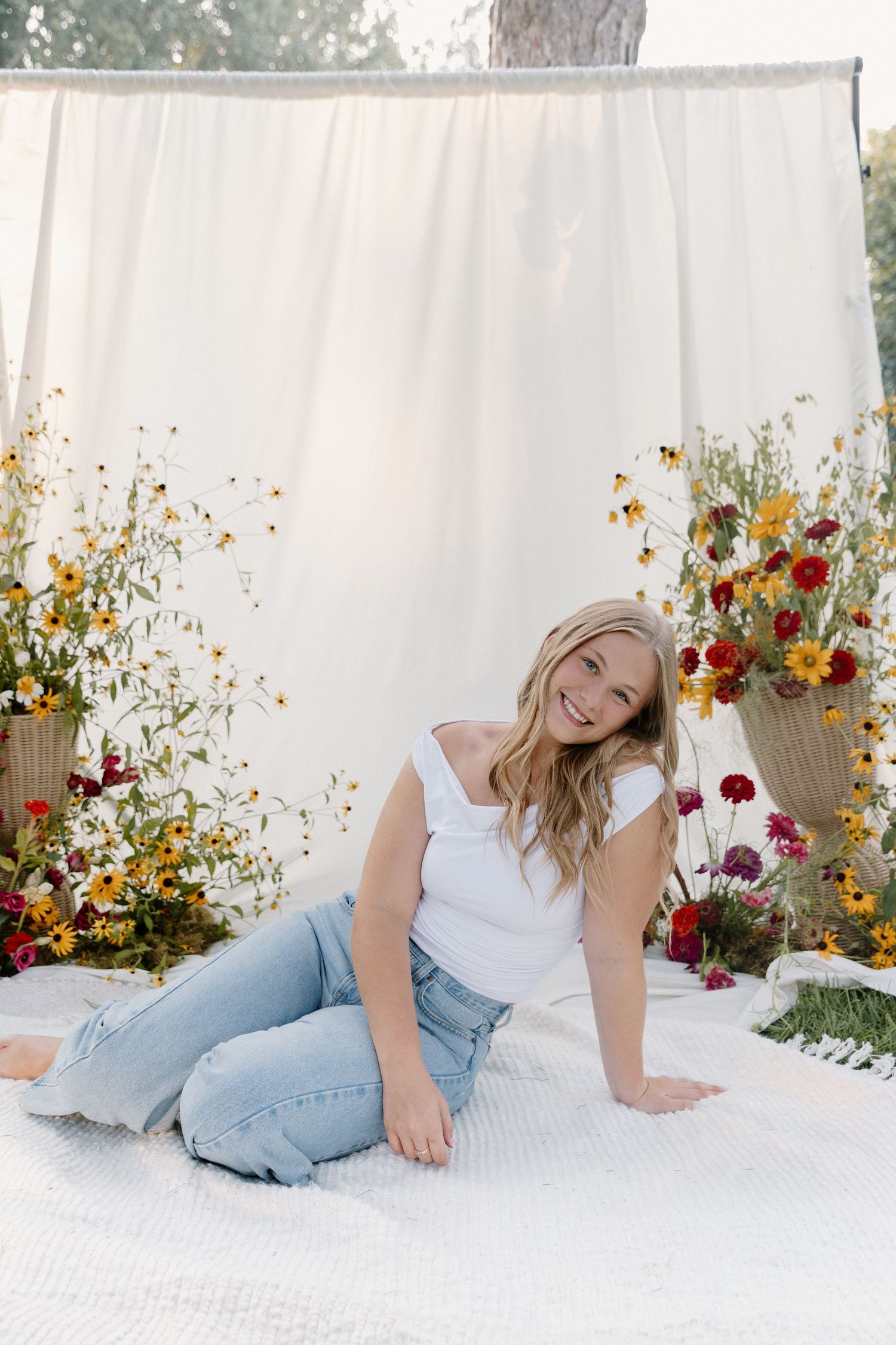 A casual outdoor photo shoot setup with white backdrop and colorful wildflower arrangements on either side.