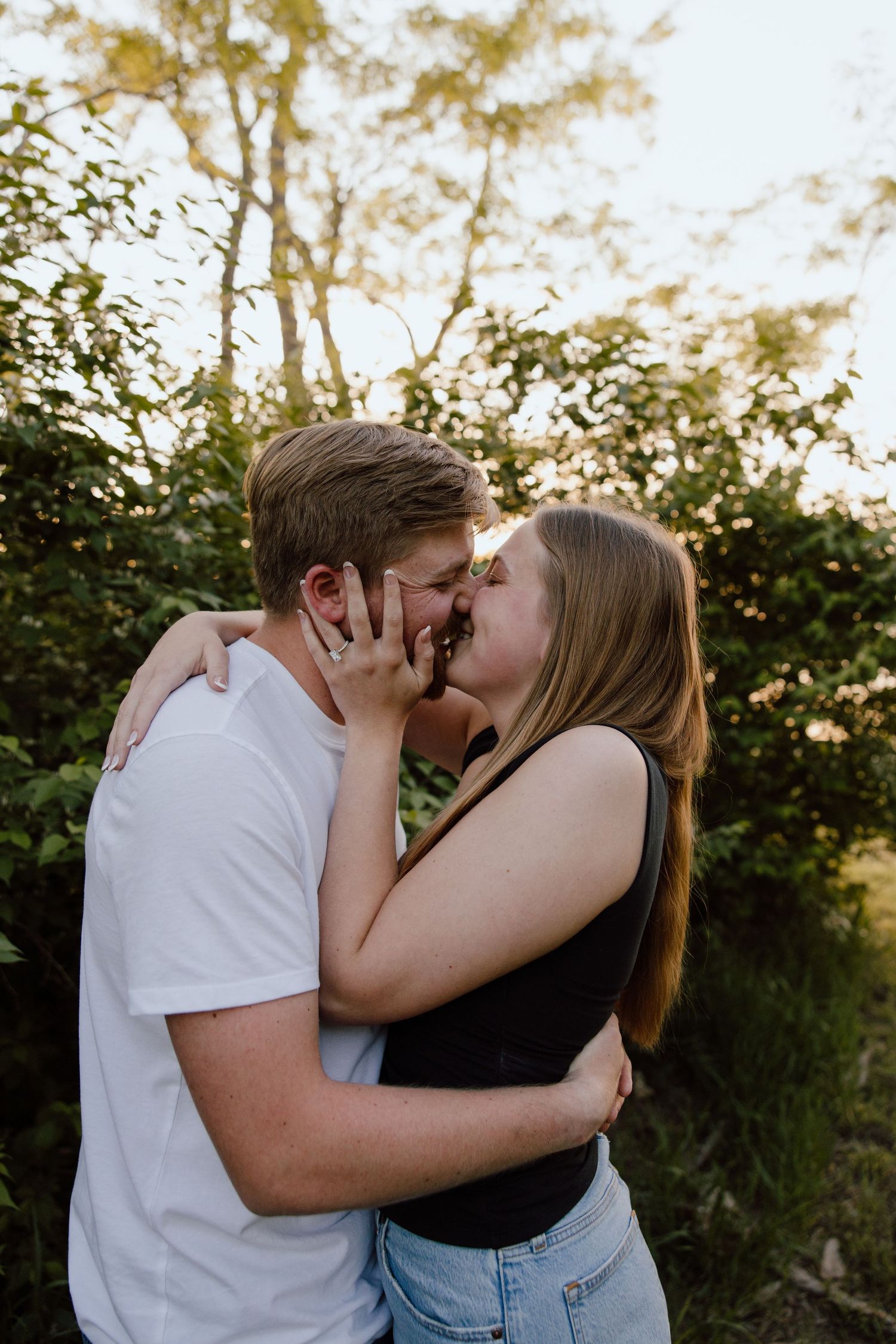 A couple shares their first kiss as newly engaged in a garden setting.