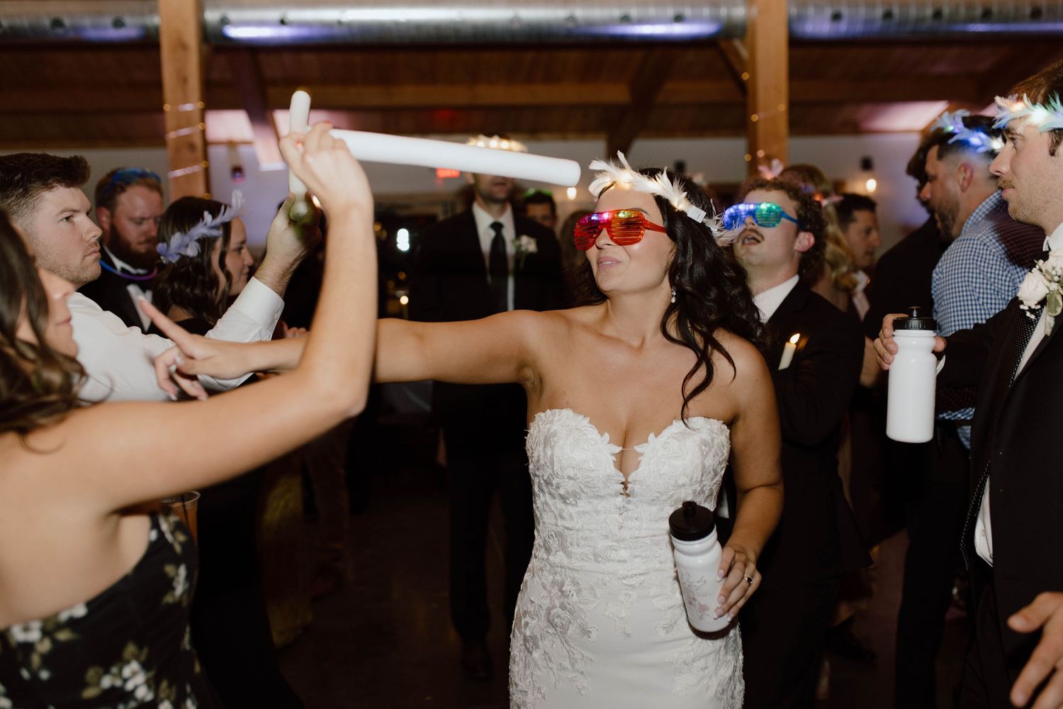 Wedding party guests dance wearing 3D glasses while a bride in a strapless white gown celebrates on the dance floor.