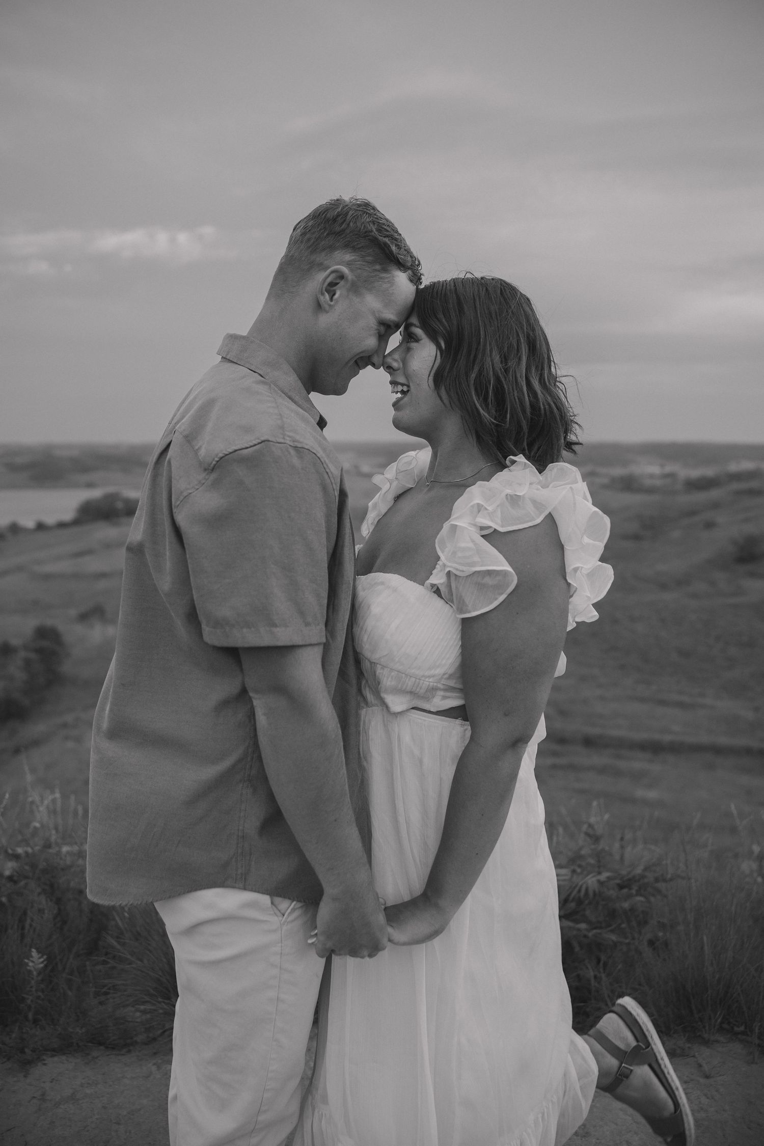 A black and white countryside portrait of a couple sharing an intimate moment on rolling hills.