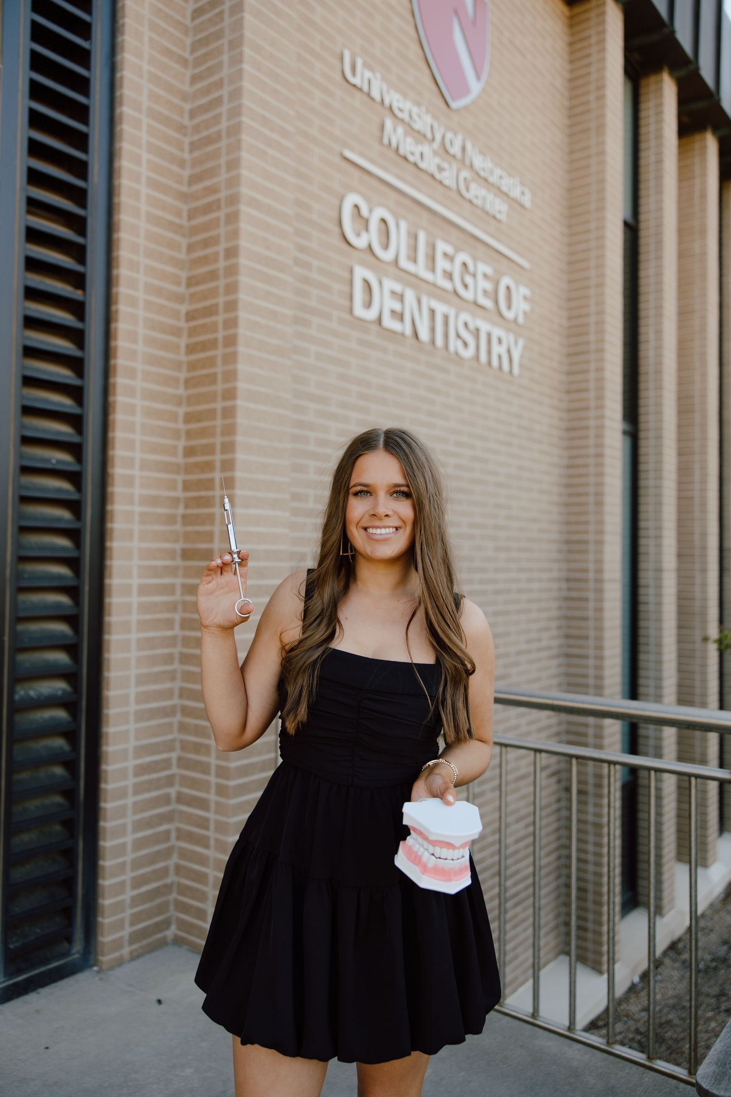A graduate poses with dental models outside the College of Dentistry building.